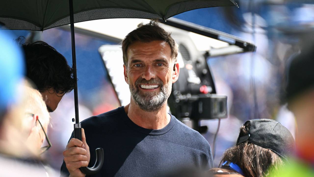 Jürgen Klopp steht als Experte bei einem Spiel zum Schutz vor der Sonne unter einem Schirm.