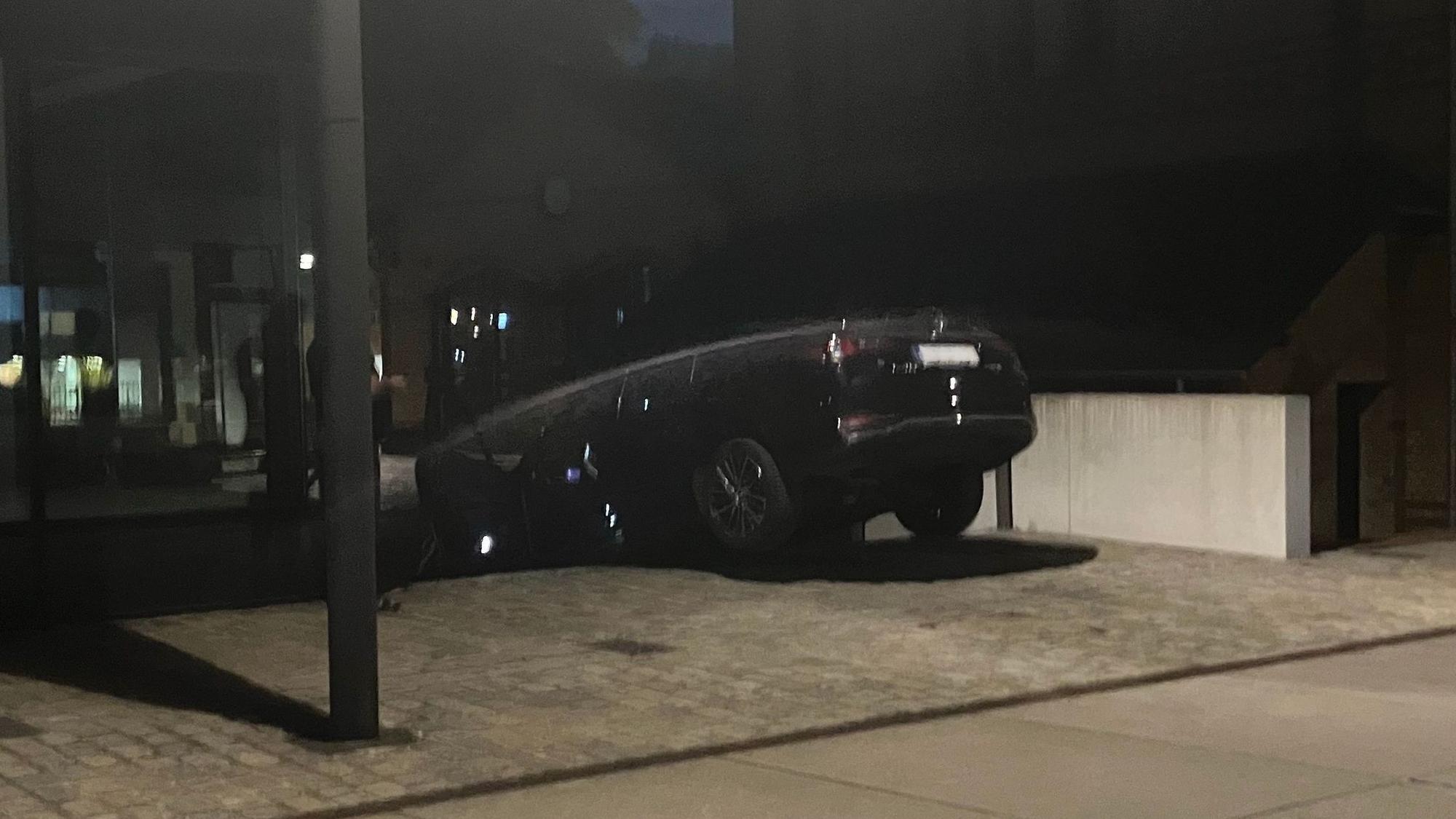 Ein dunkles Auto hängt halb in einem Treppenabgang.