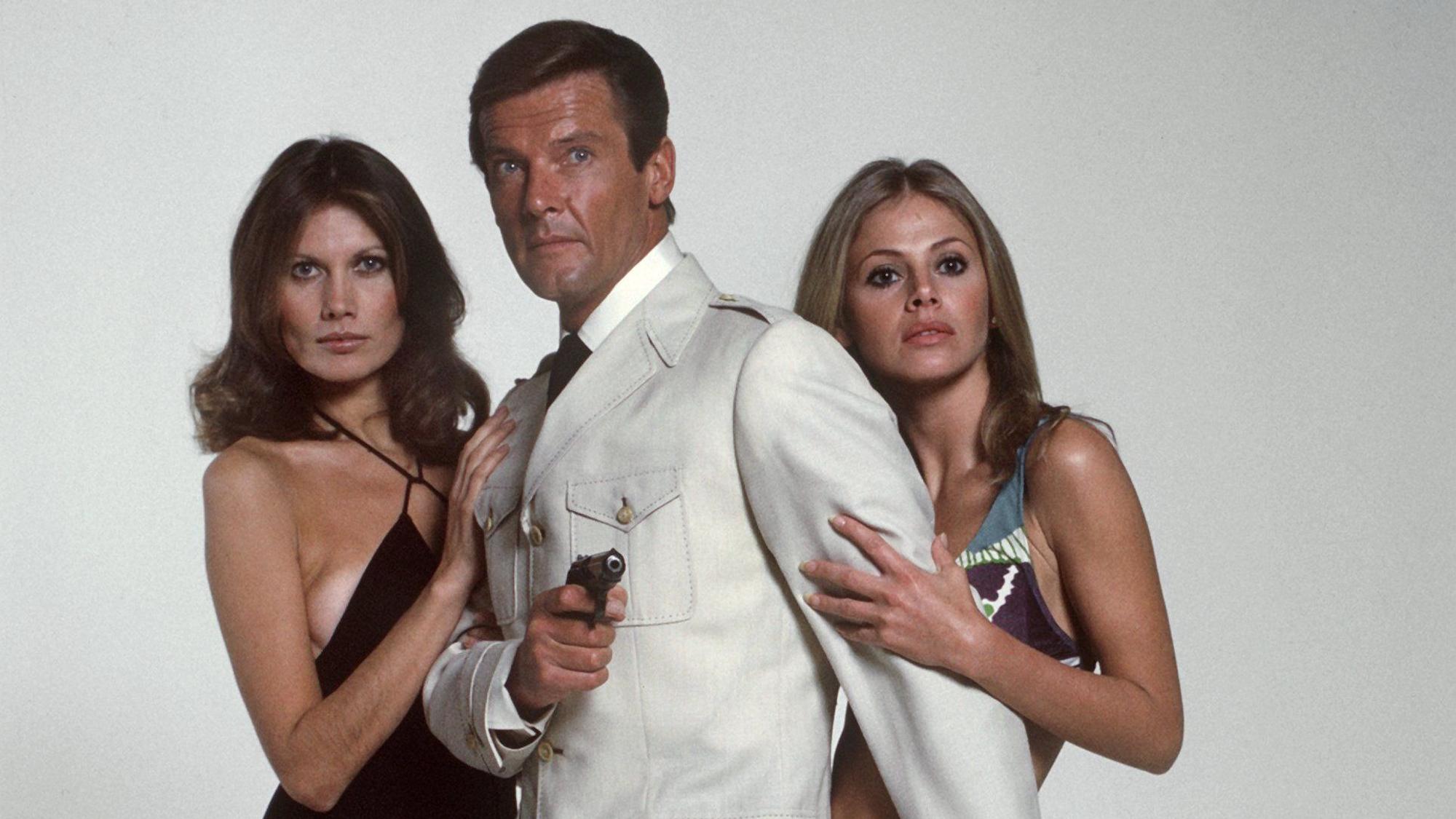 Das Archivbild von 1972 zeigt den dritten „James Bond“-Darsteller Roger Moore mit den Bond-Girls Maude Adams (l) und Britt Ekland im Film „Der Mann mit dem goldenen Colt“.