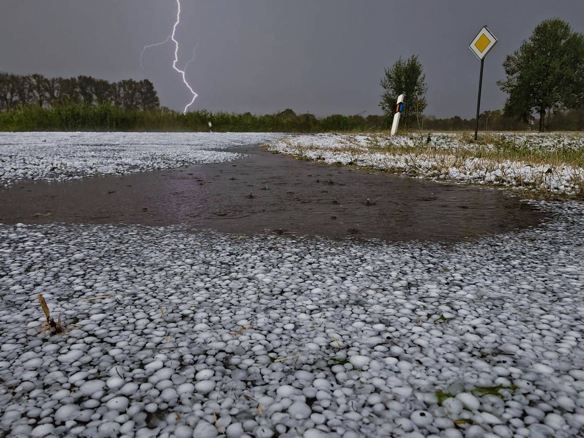 Schwere Unwetter sind über Teilen Niedersachsens niedergegangen. Hagelkörner liegen auf einer Fahrbahn bei Wagenfeld in Niedersachsen, während sich ein Blitz im Hintergrund entlädt.