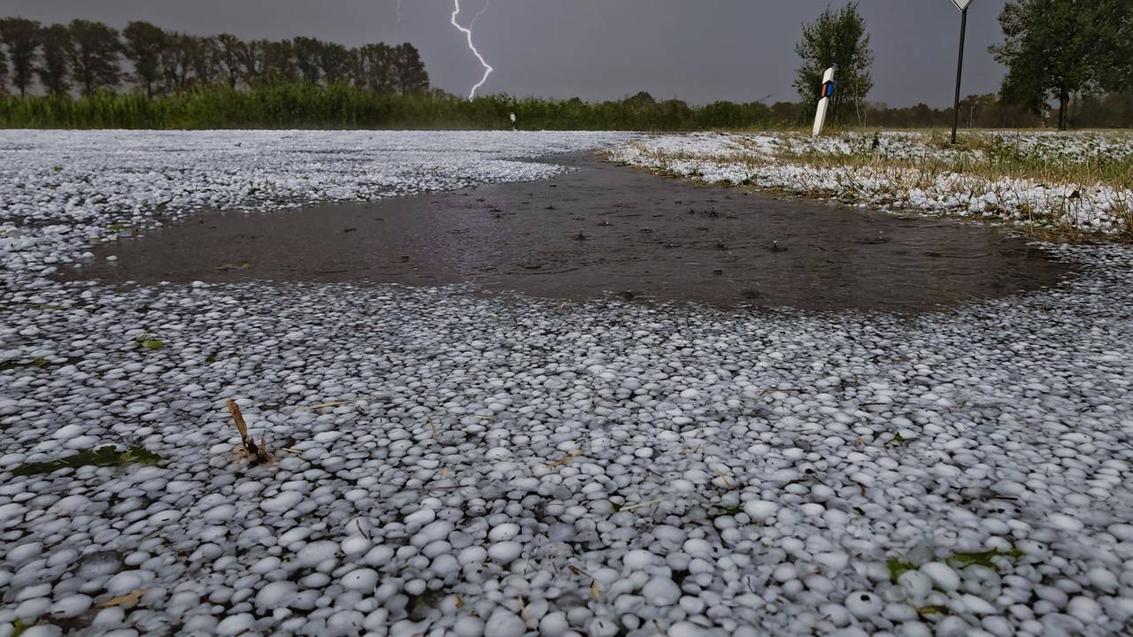Schwere Unwetter sind über Teilen Niedersachsens niedergegangen. Hagelkörner liegen auf einer Fahrbahn bei Wagenfeld in Niedersachsen, während sich ein Blitz im Hintergrund entlädt.