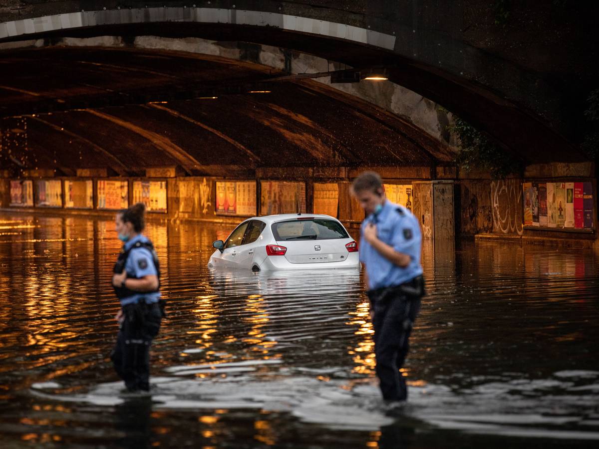 Eine Unterführung ist überflutet, ein Auto steht bis zur Hälfte im Wasser, einem Polizist und einer Polizistin reicht das Wasser fast bis zu den Knien.