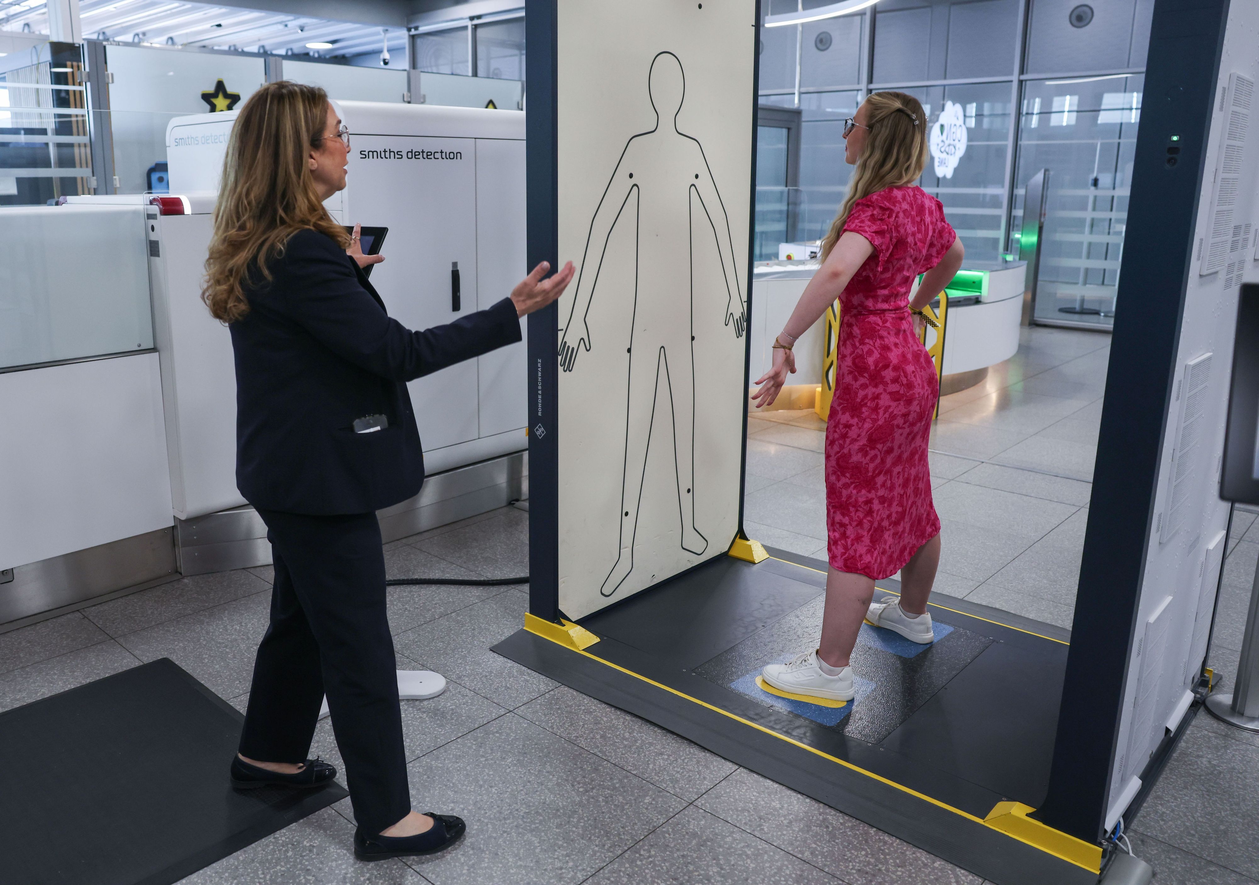 Die Mitarbeiterin einer Sicherheitsfirma leitet im Sicherheitsbereich am Flughafen Köln/Bonn eine Reisende in einen Körperscanner. Eine neue Anlage mit elf modernen CT-Kontrollspuren und Scannern soll künftig für schnellere, komfortablere und effizientere Abläufe sorgen.