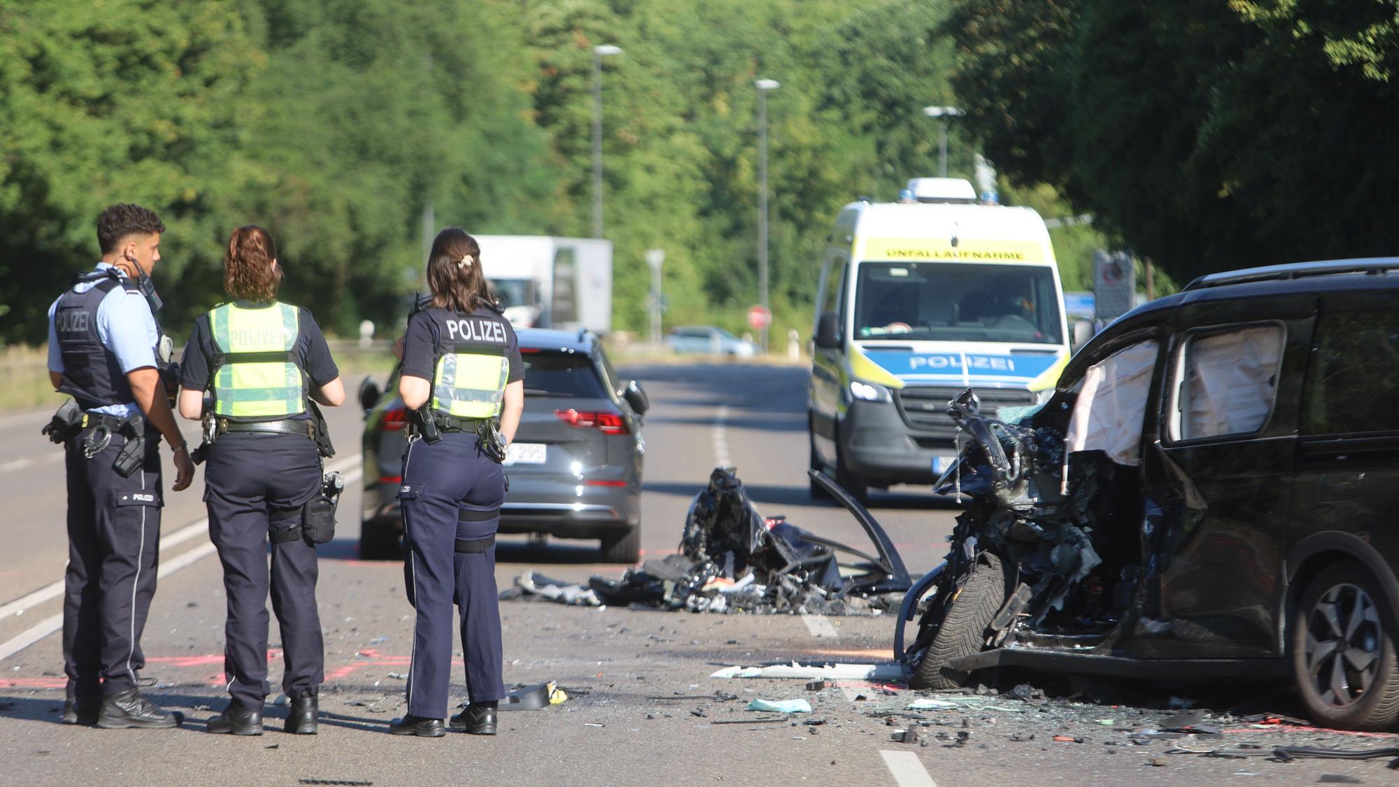Einsatzkräfte der Polizei stehen am Mittwochmorgen (15. Juli 2026) an der Unfallstelle. Nach dem Frontalcrash liegen zahlreiche Trümmerteile auf den Fahrbahnen der Kölner Straße.