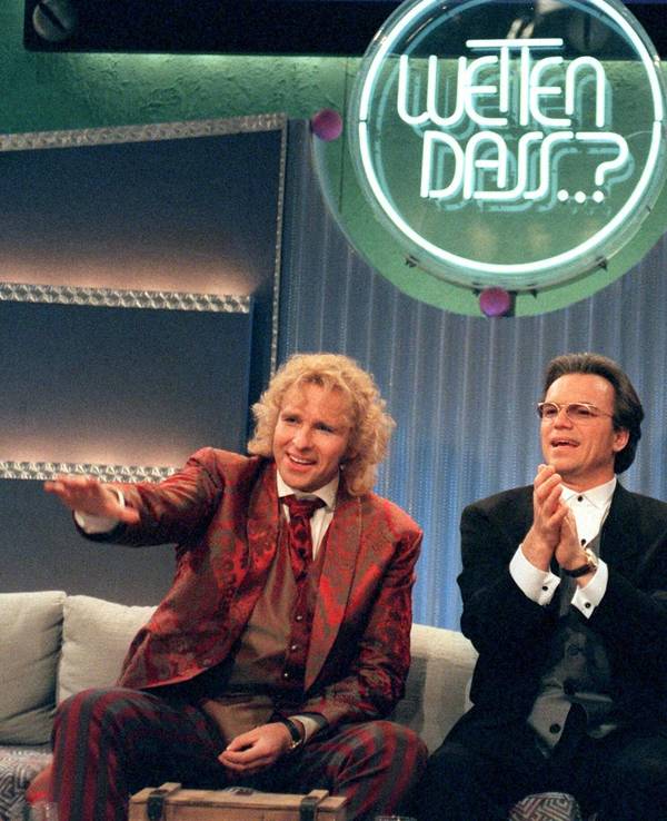 Drei schick gekleifdete Herren albern auf einem Sofa unter dem Logo von "Wetten, dass..?!" herum.