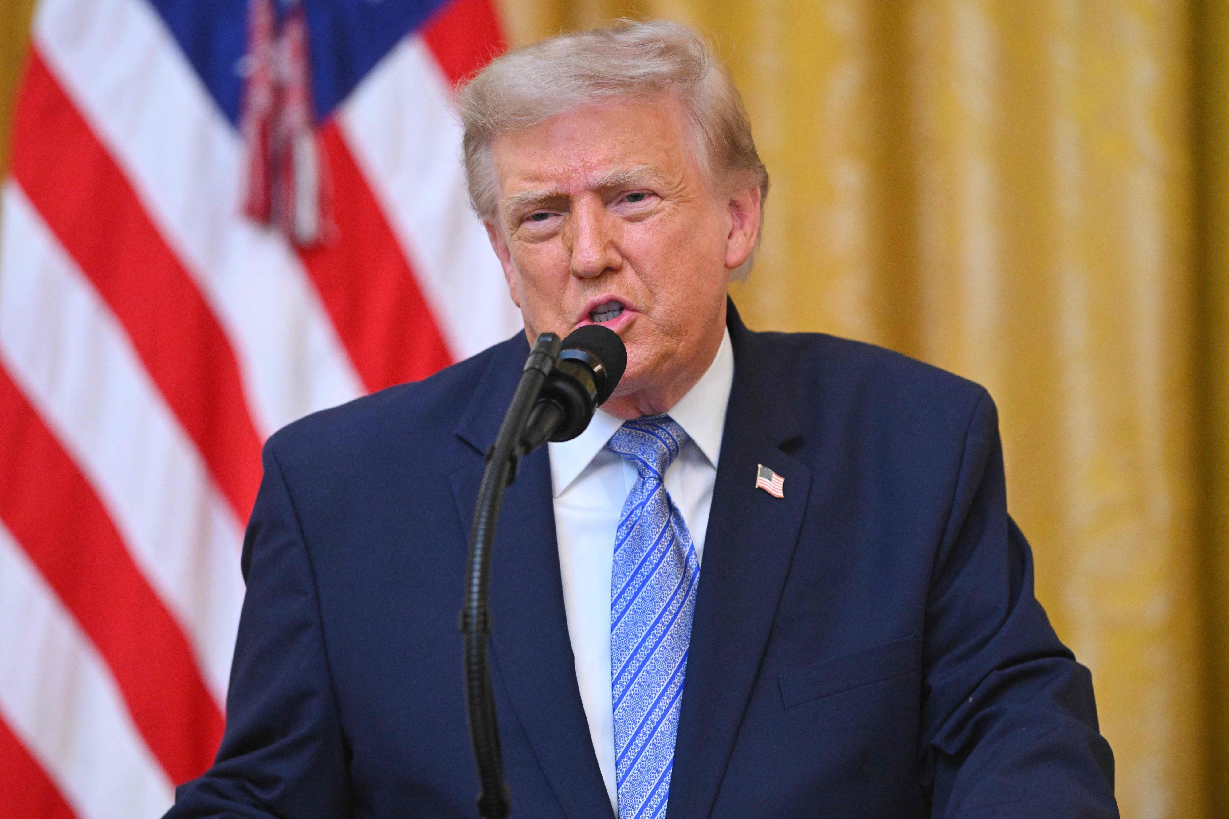 Donald Trump spricht bei einer Rede an die Nation in ein Mikrofon, im Hintergrund die US-Flagge.