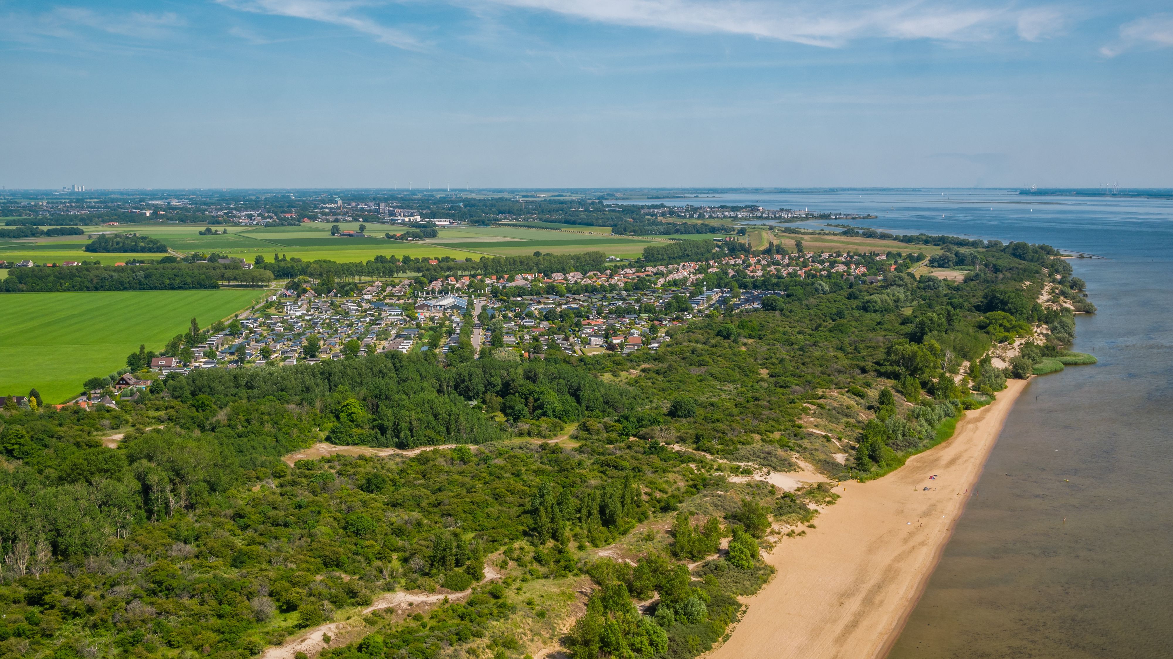 Ein Strand mit einer Feriensiedlung in einem kleinen Waldstück