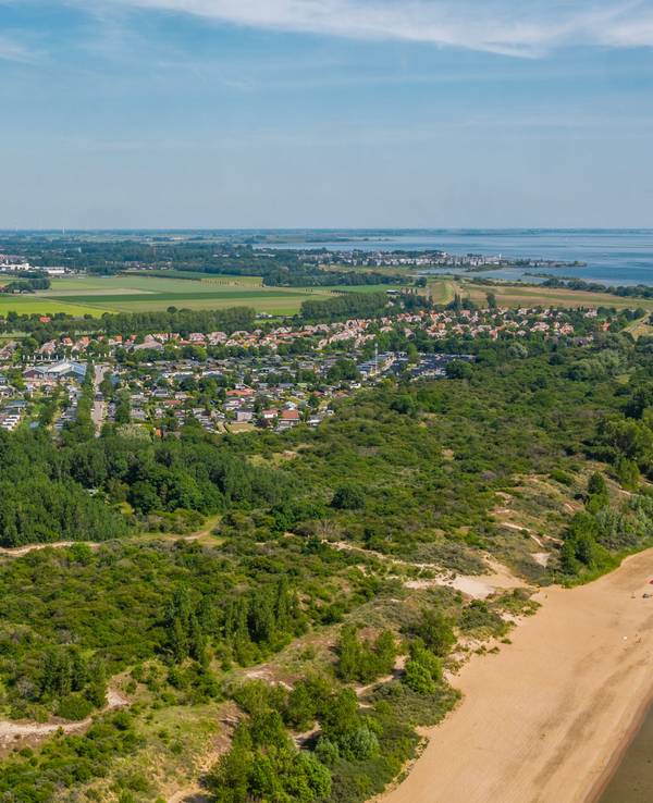 Ein Strand mit einer Feriensiedlung in einem kleinen Waldstück