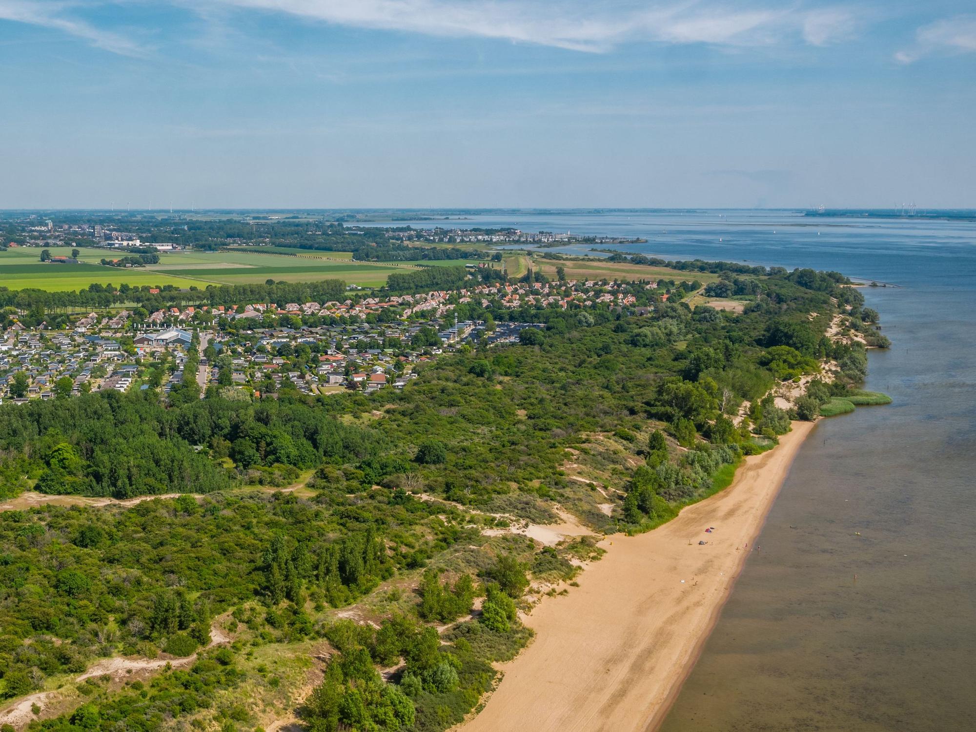 Ein Strand mit einer Feriensiedlung in einem kleinen Waldstück