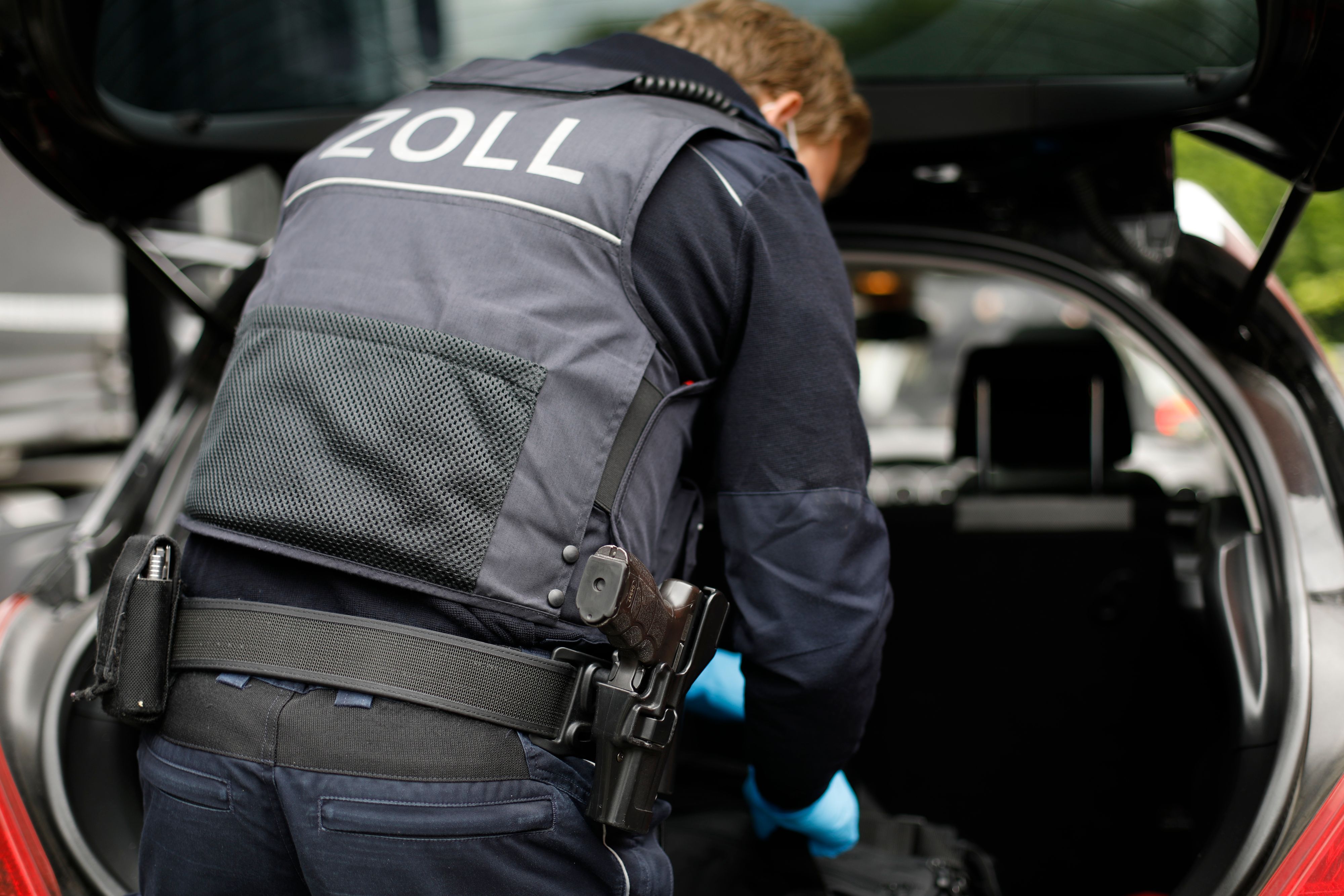 Ein Beamter des Zolls verstaut etwas im Kofferraum eines Fahrzeugs.