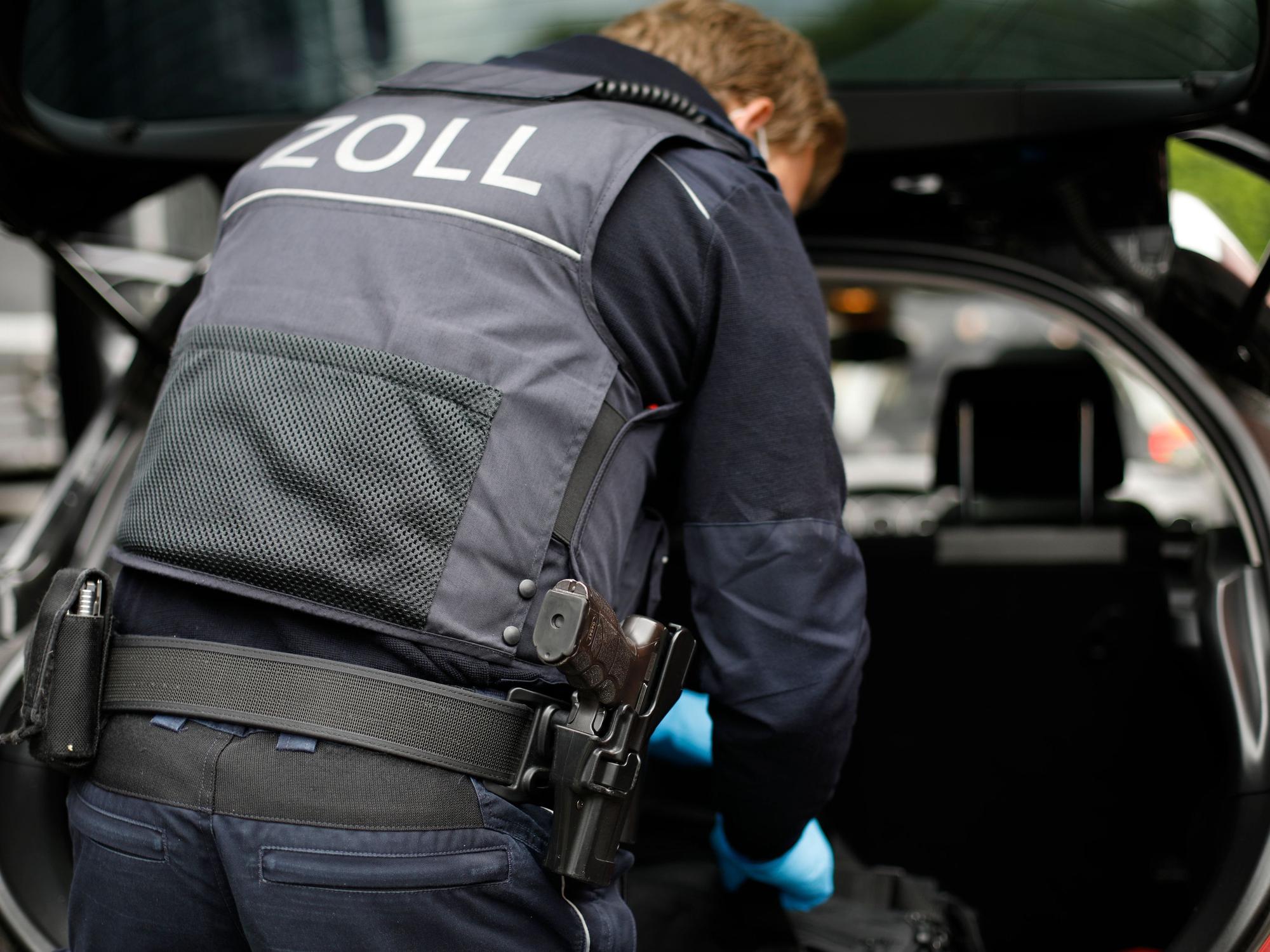 Ein Beamter des Zolls verstaut etwas im Kofferraum eines Fahrzeugs.