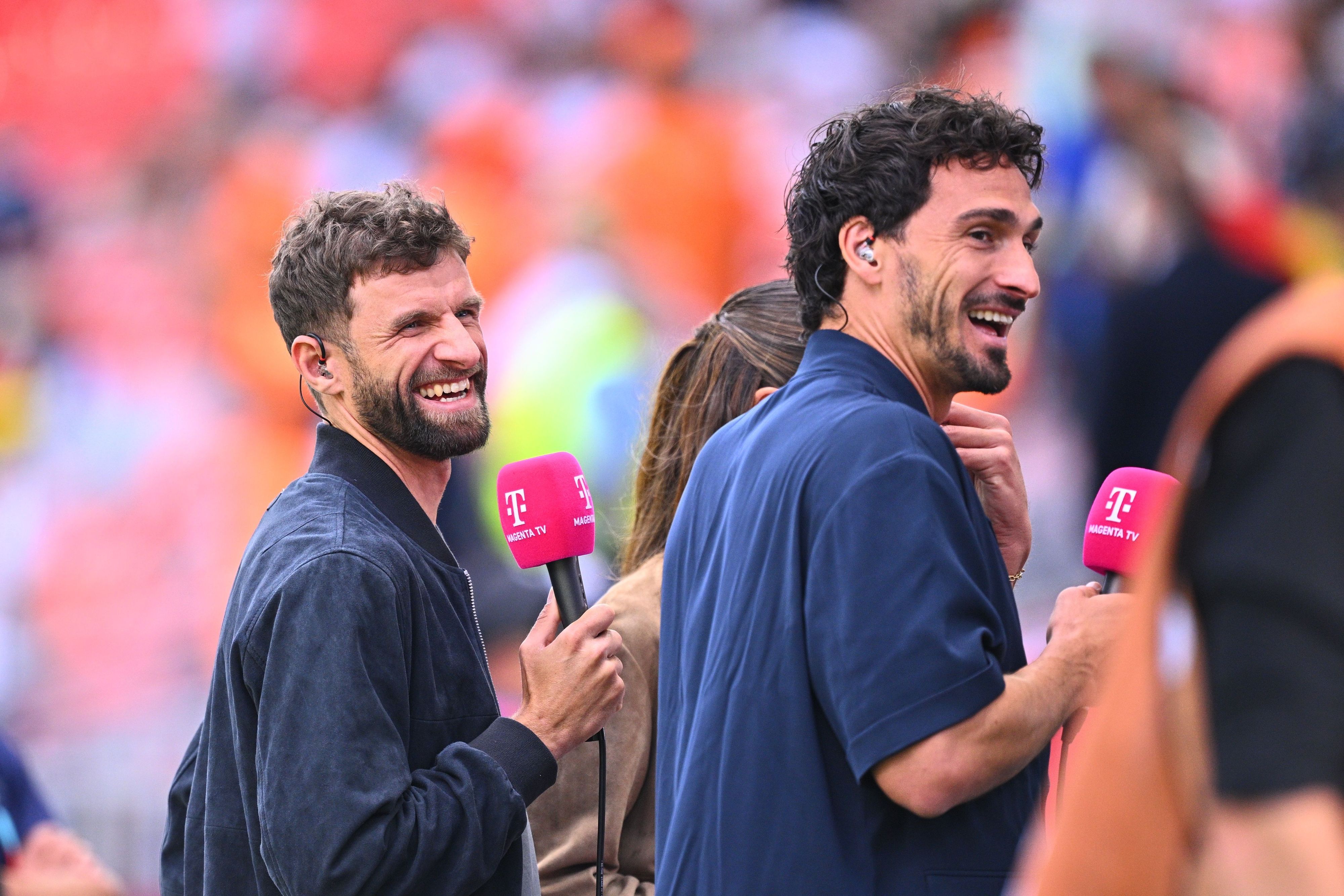 Thomas Müller und Mats Hummels lachen mit MagentaTV-Mikros in der Hand.