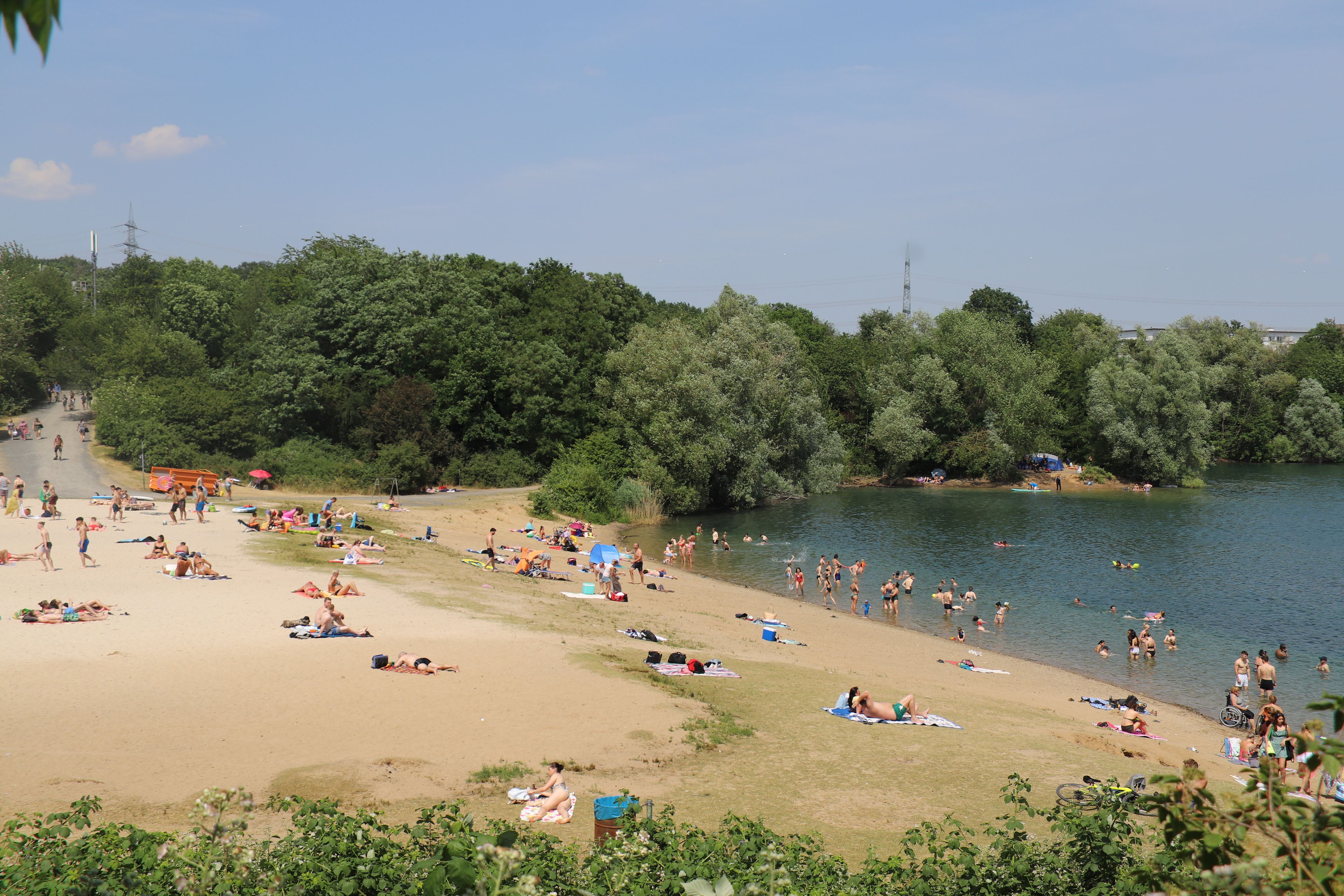 Menschen liegen am Ufer des Rotter Sees, andere plantschen im Wasser.