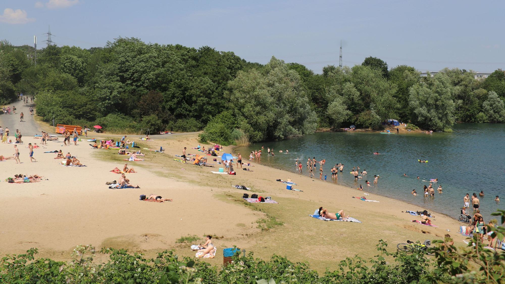 Menschen liegen am Ufer des Rotter Sees, andere plantschen im Wasser.