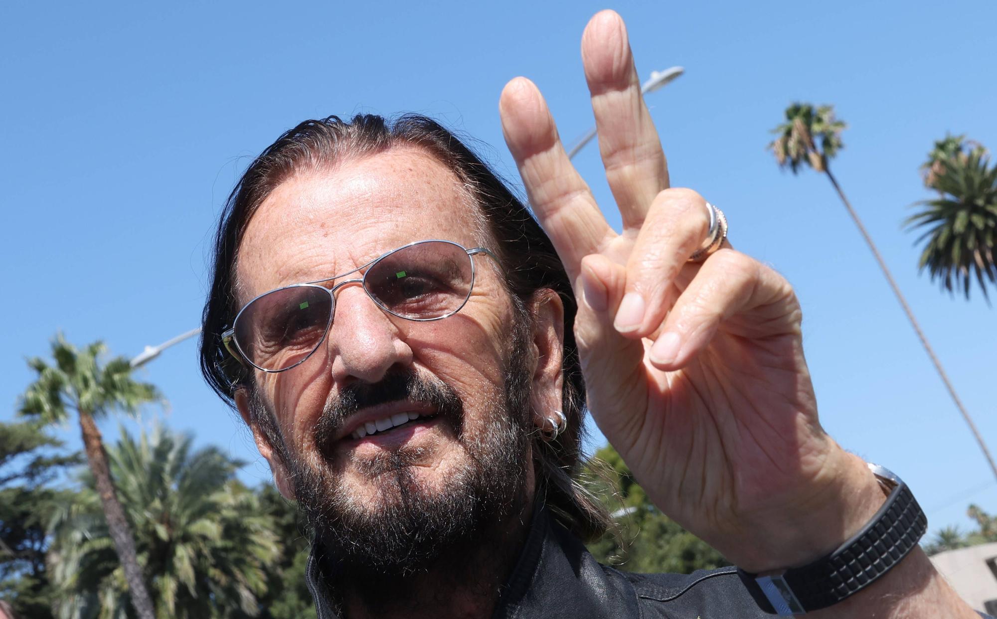 Ringo Starr macht ein Peace-Zeichen.