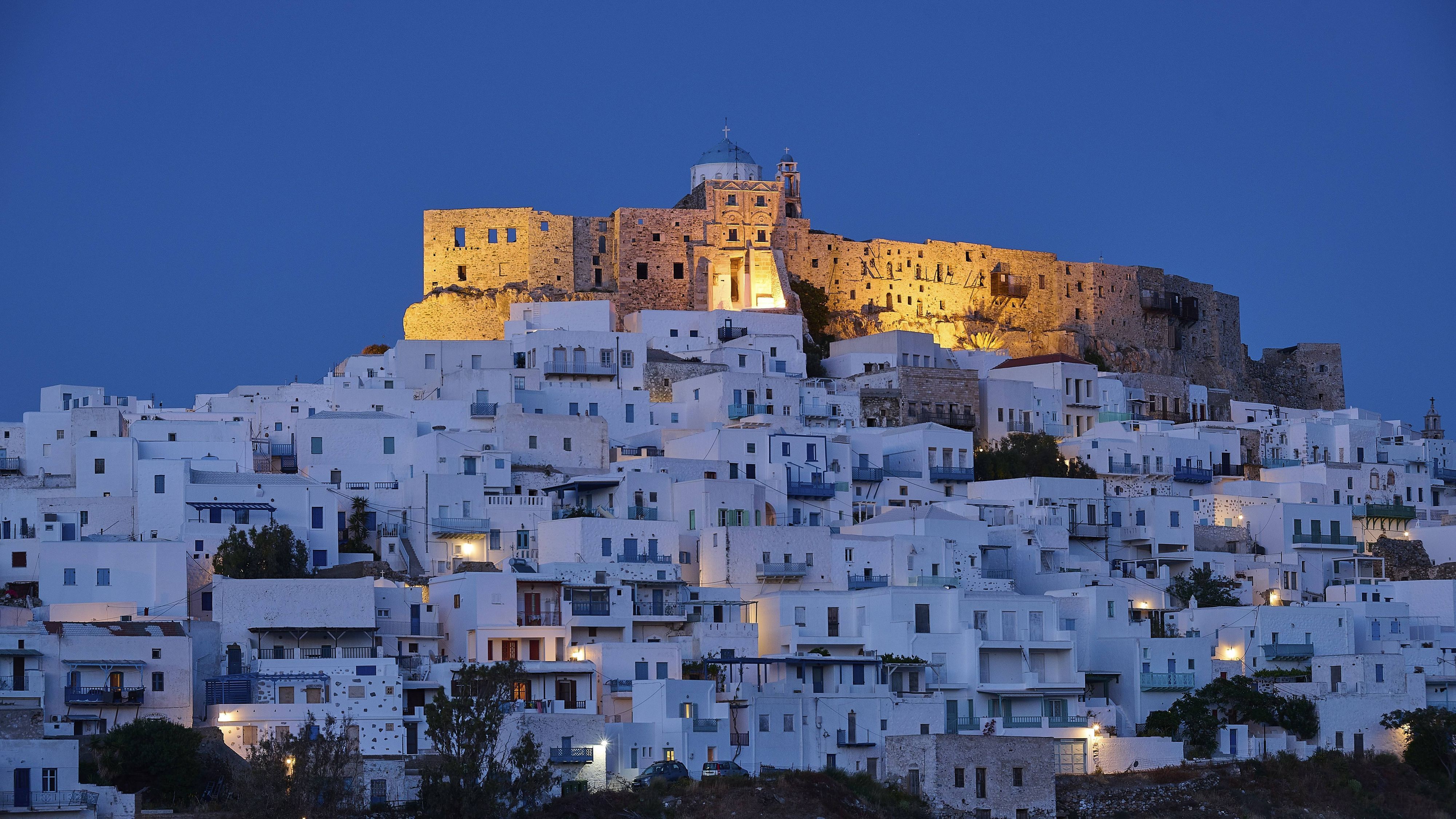 Nächtlicher Blick auf die beleuchtete Burg Querini über den weiß getünchten Häusern von Chora auf der griechischen Insel Astypalea.