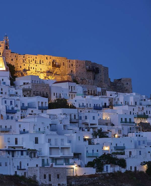 Nächtlicher Blick auf die beleuchtete Burg Querini über den weiß getünchten Häusern von Chora auf der griechischen Insel Astypalea.