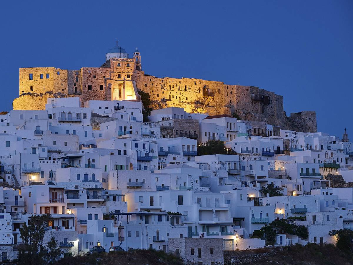 Nächtlicher Blick auf die beleuchtete Burg Querini über den weiß getünchten Häusern von Chora auf der griechischen Insel Astypalea.