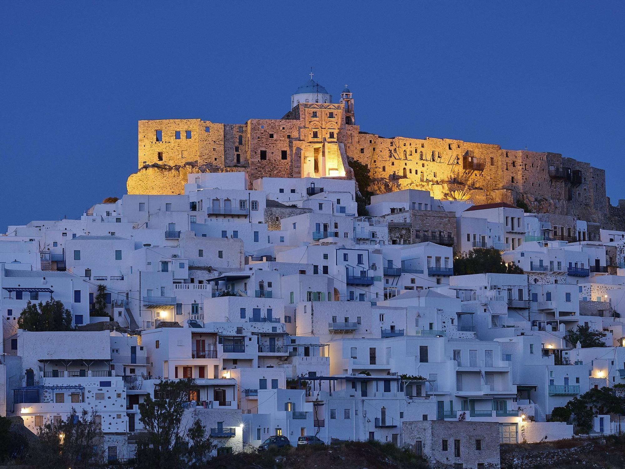 Nächtlicher Blick auf die beleuchtete Burg Querini über den weiß getünchten Häusern von Chora auf der griechischen Insel Astypalea.