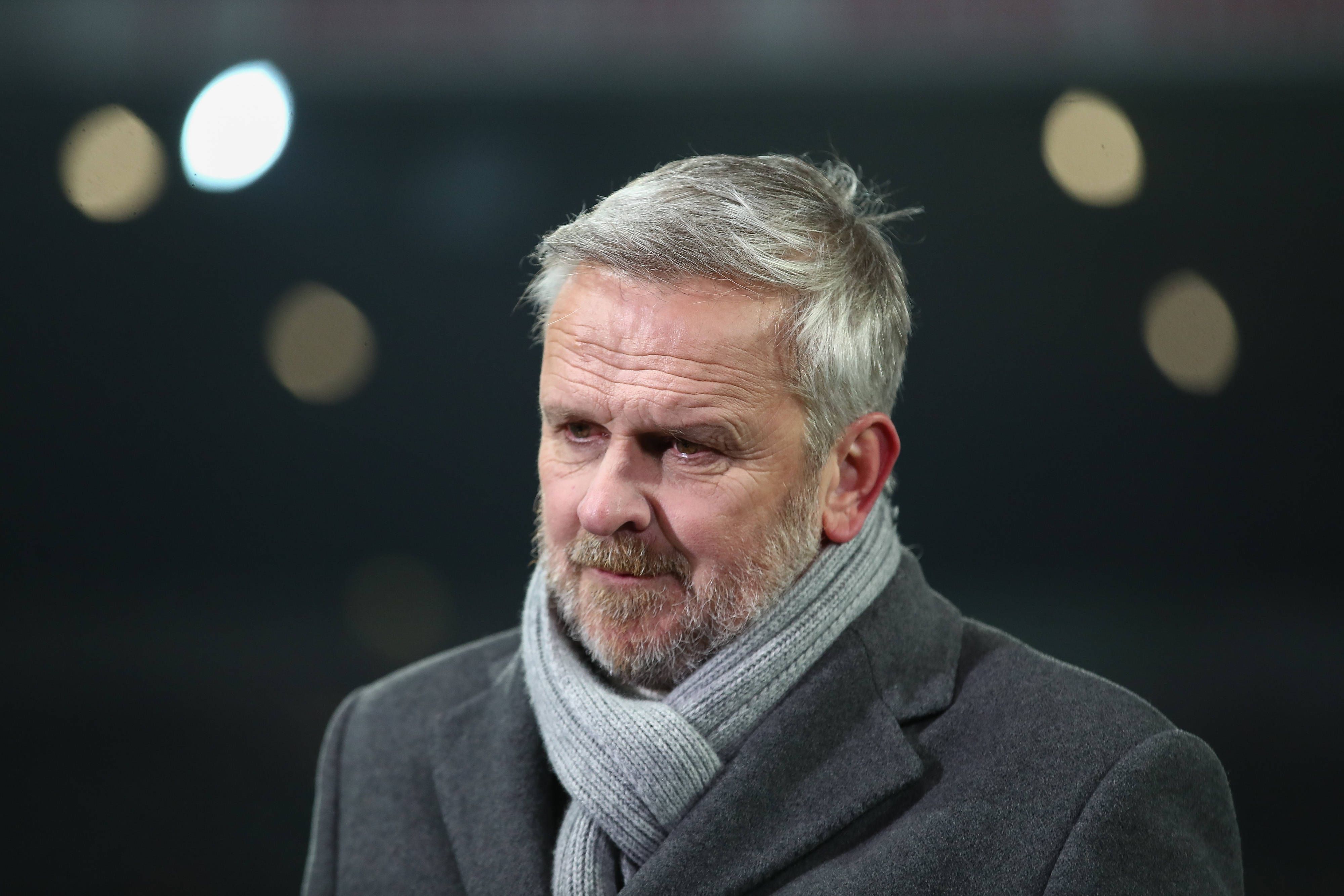 Dietmar Hamann trägt einen Schal und einen Mantel und steht im Stadion.