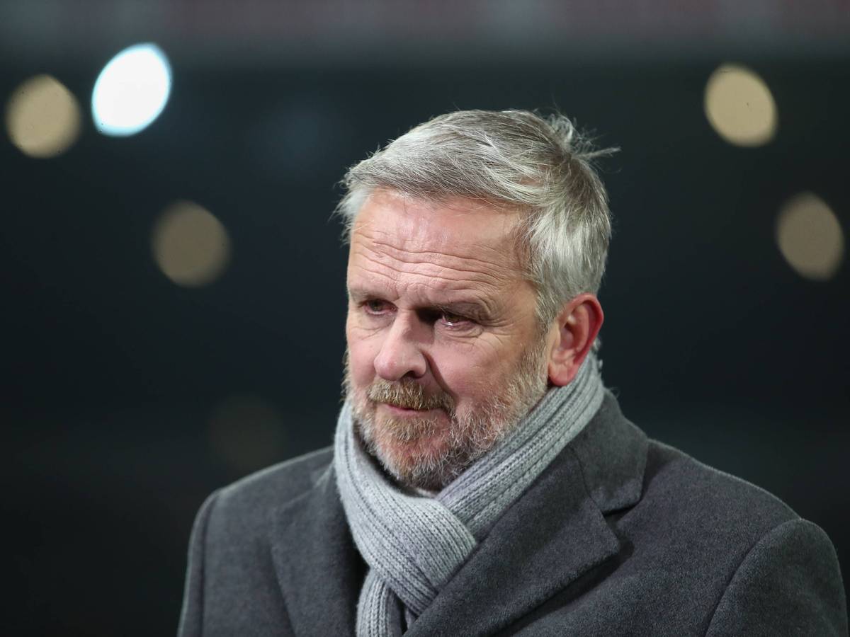 Dietmar Hamann trägt einen Schal und einen Mantel und steht im Stadion.