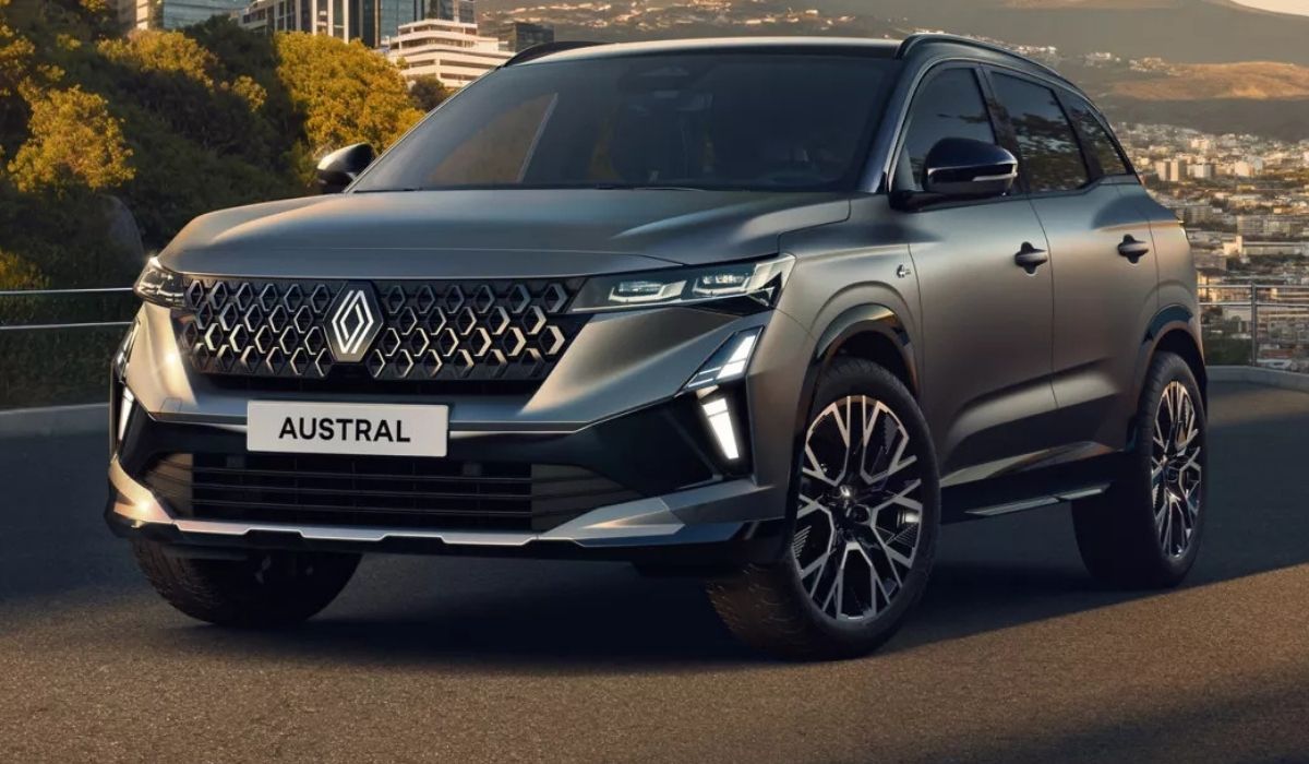 Hybrid-SUV Renault Austral Evolution in Silber-Grau auf einer Straße vor einer Stadtkulisse.