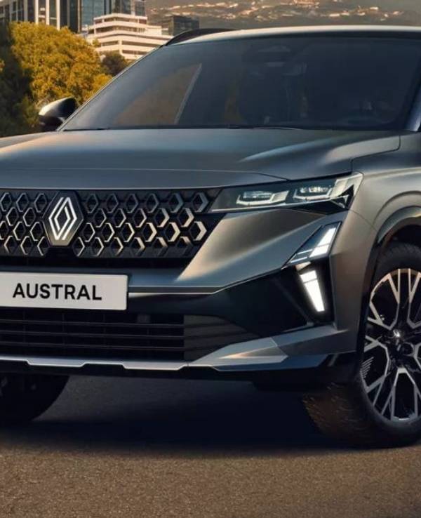 Hybrid-SUV Renault Austral Evolution in Silber-Grau auf einer Straße vor einer Stadtkulisse.
