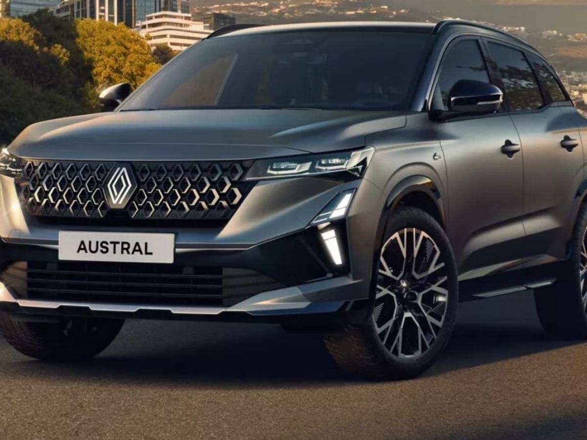 Hybrid-SUV Renault Austral Evolution in Silber-Grau auf einer Straße vor einer Stadtkulisse.