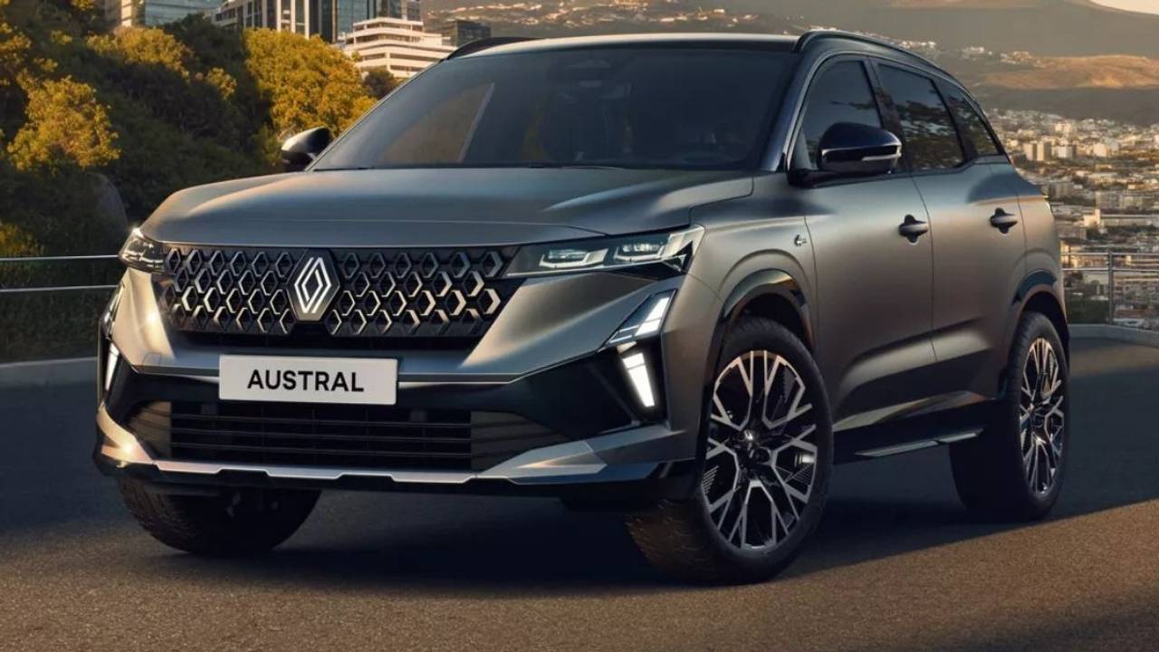 Hybrid-SUV Renault Austral Evolution in Silber-Grau auf einer Straße vor einer Stadtkulisse.