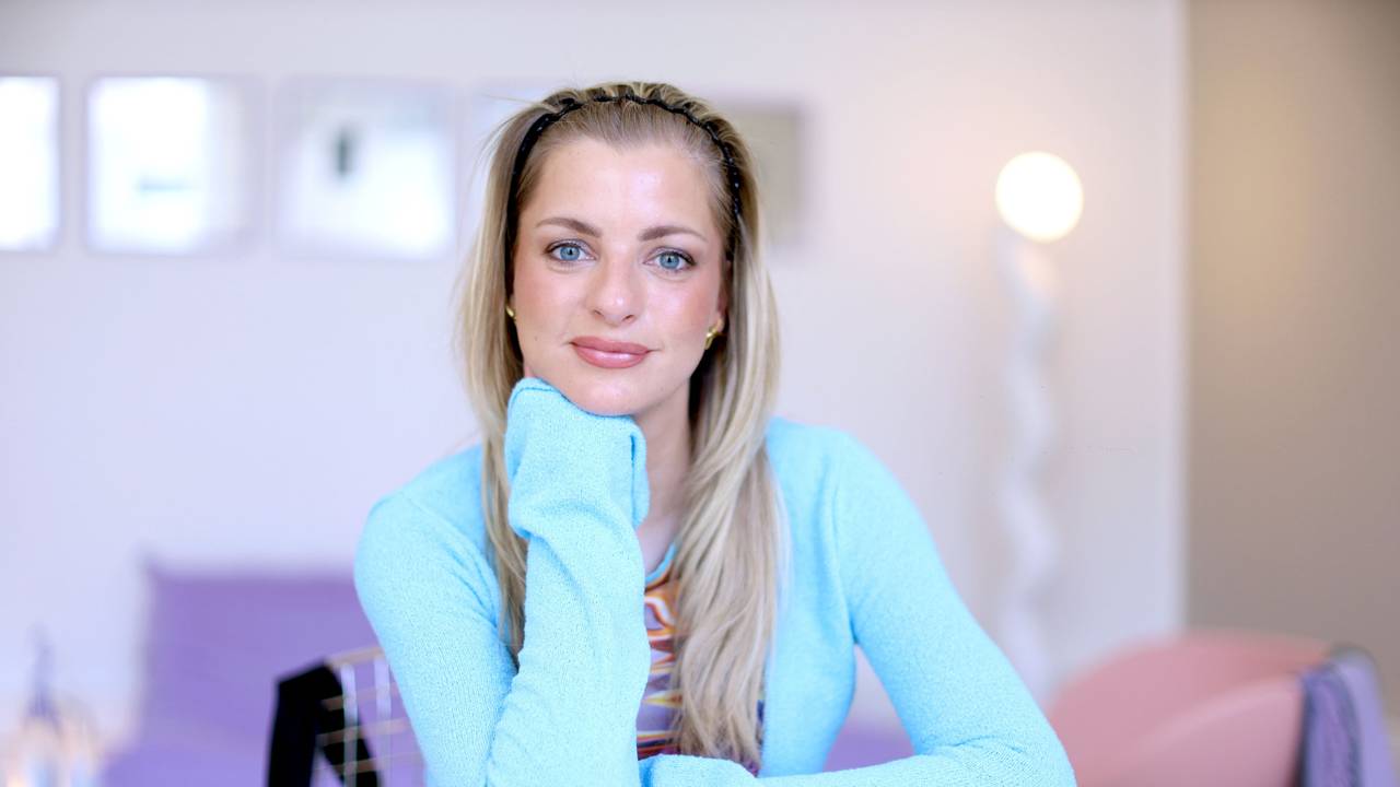 Eine blonde Frau mit langen Haaren hat ihren Kopf in die Hand gestützt und lächelt