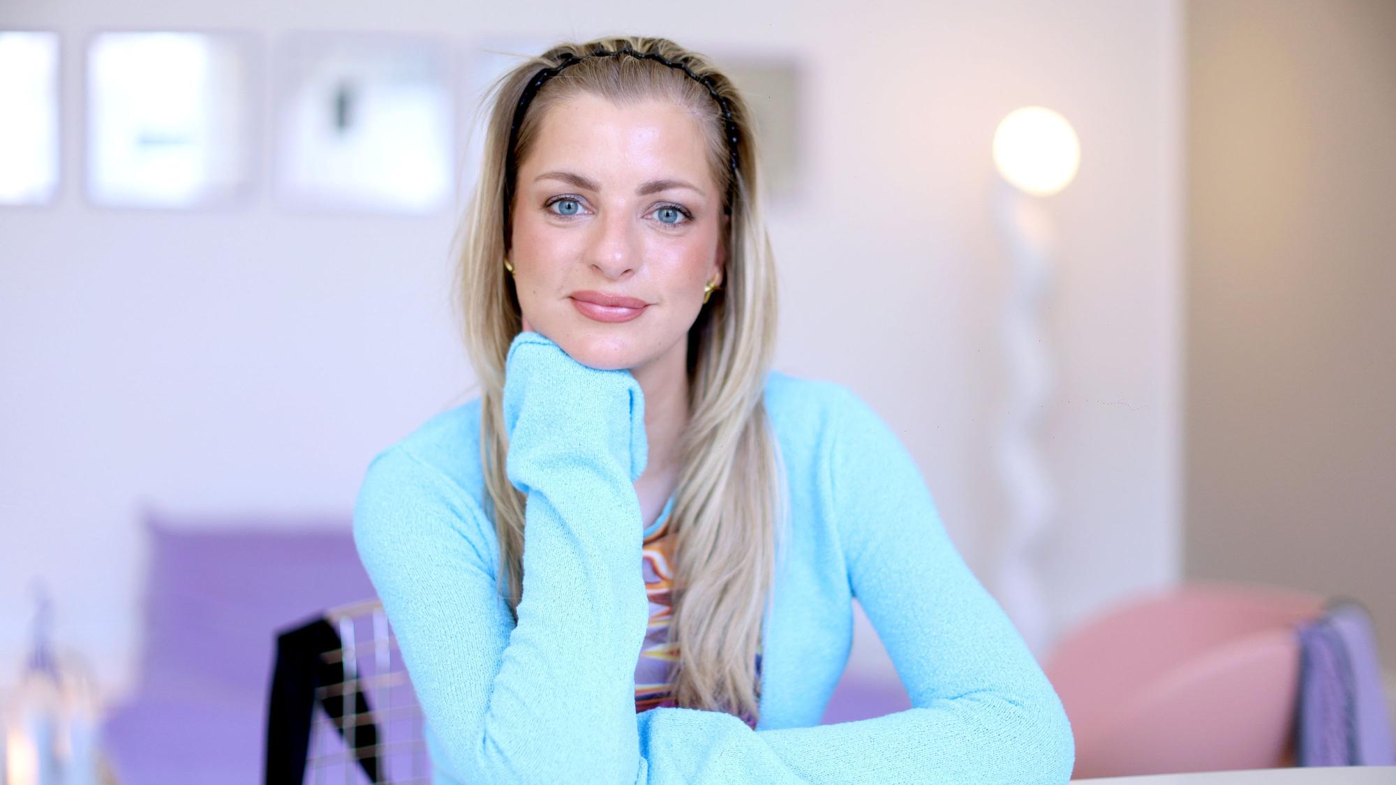 Eine blonde Frau mit langen Haaren hat ihren Kopf in die Hand gestützt und lächelt