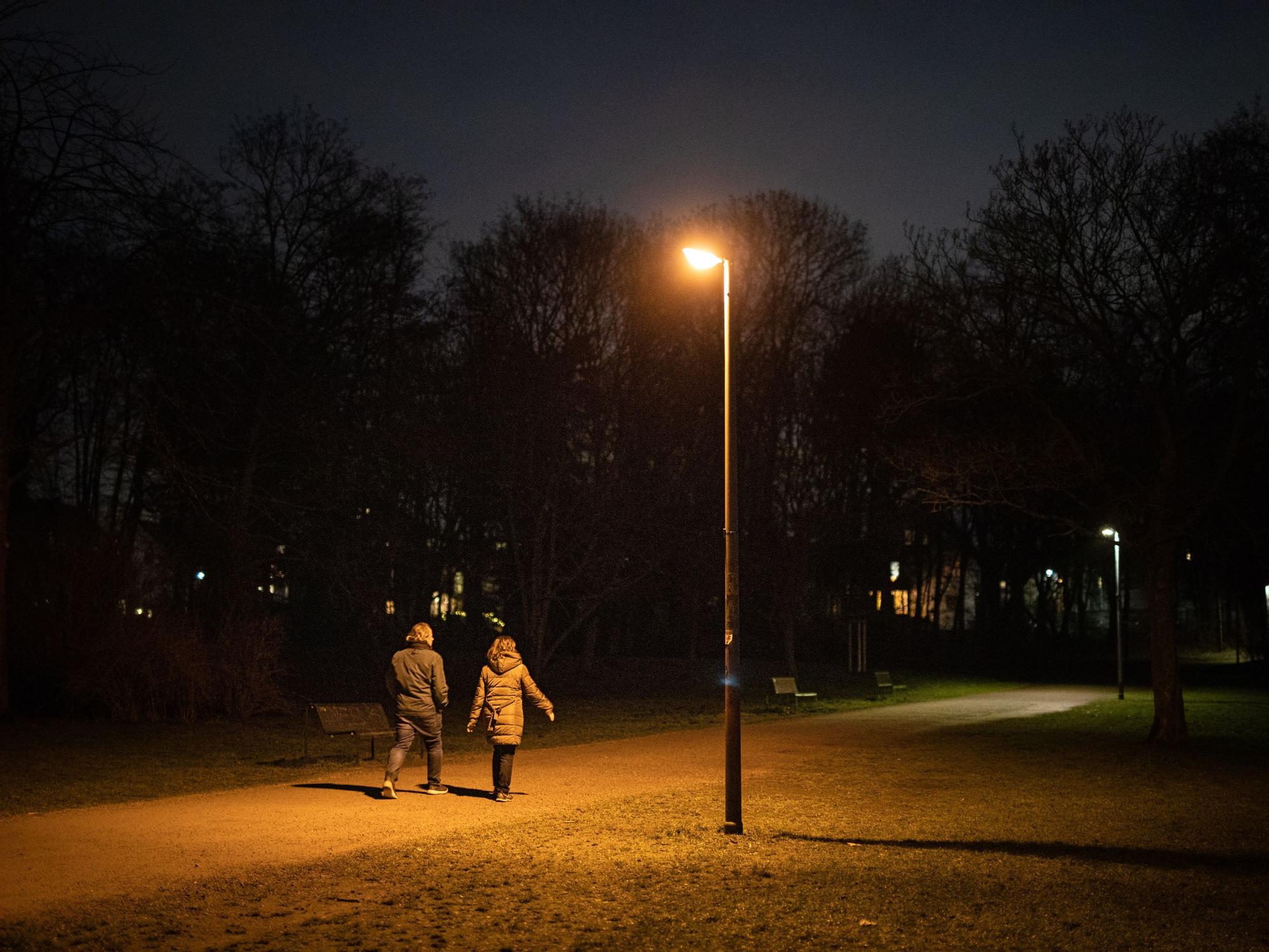 Zwei Personen sind am Abend auf einem Weg im dunklen Beethovenpark unterwegs, während eine Straßenlaterne leuchtet.