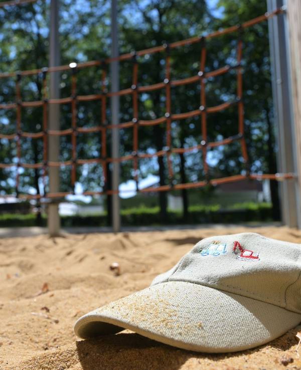 Im Sand eines Spielplatzes liegt eine Mütze.