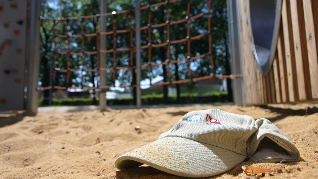 Im Sand eines Spielplatzes liegt eine Mütze.