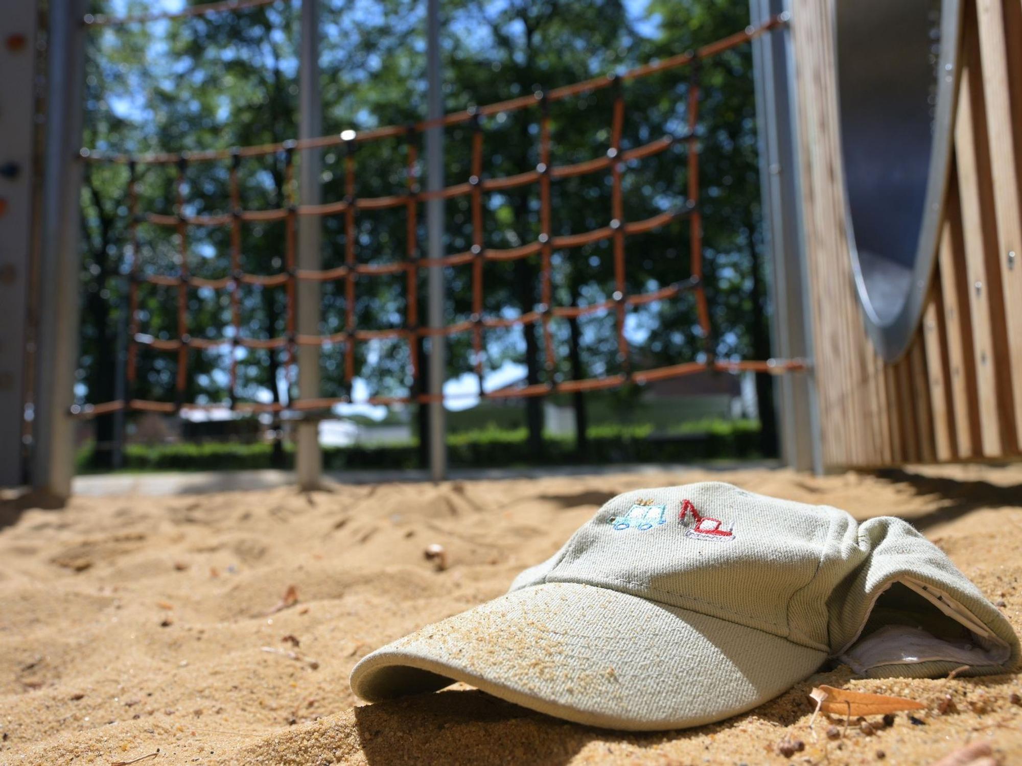 Im Sand eines Spielplatzes liegt eine Mütze.