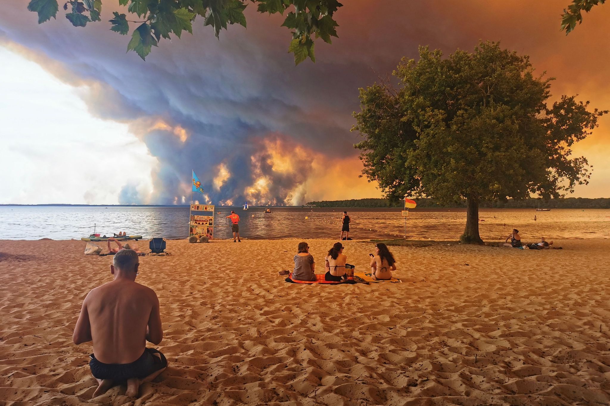 Touristen und Touristinnen beobachten vom Strand aus das Feuer. Noch ist der beliebte Urlaubsort Lacanau (Frankreich) nicht direkt von dem Waldbrand bedroht.