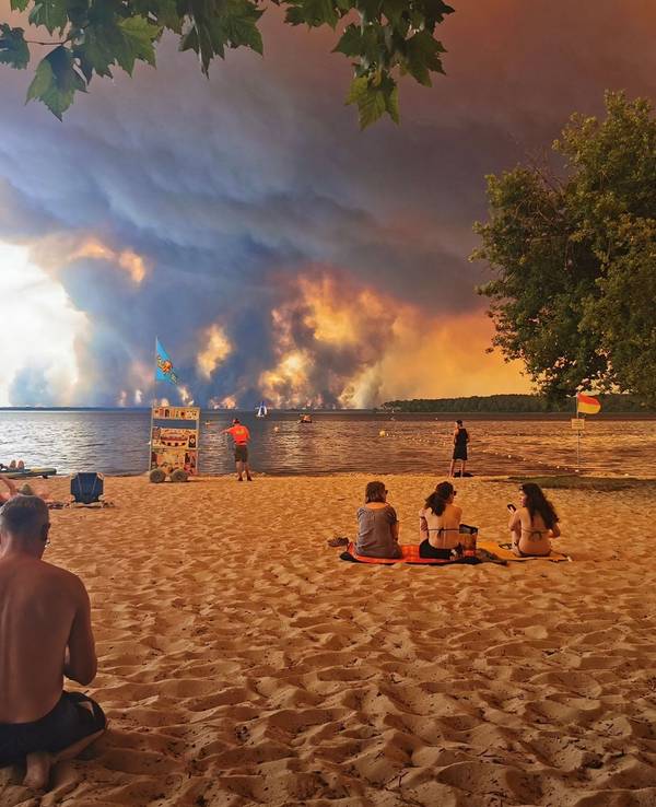 Touristen und Touristinnen beobachten vom Strand aus das Feuer. Noch ist der beliebte Urlaubsort Lacanau (Frankreich) nicht direkt von dem Waldbrand bedroht.