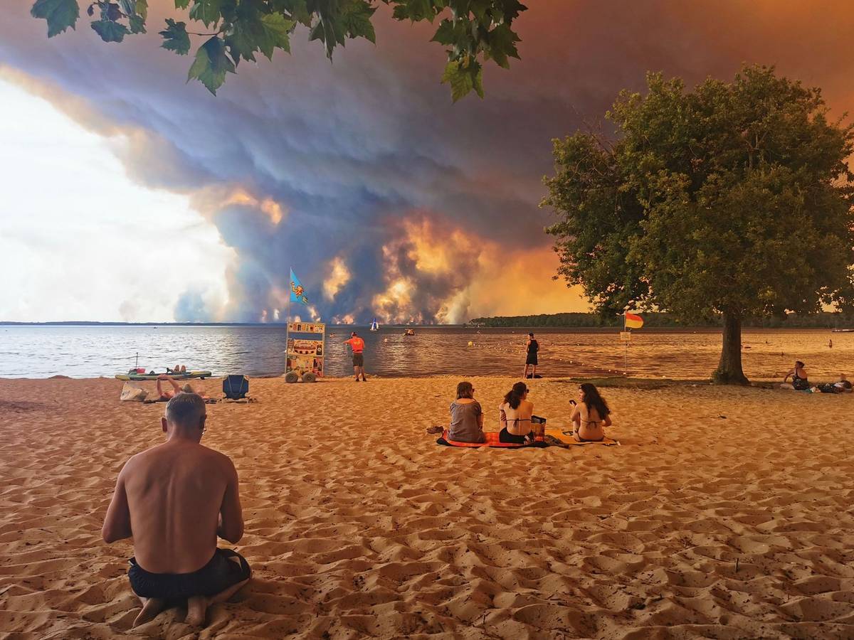 Touristen und Touristinnen beobachten vom Strand aus das Feuer. Noch ist der beliebte Urlaubsort Lacanau (Frankreich) nicht direkt von dem Waldbrand bedroht.