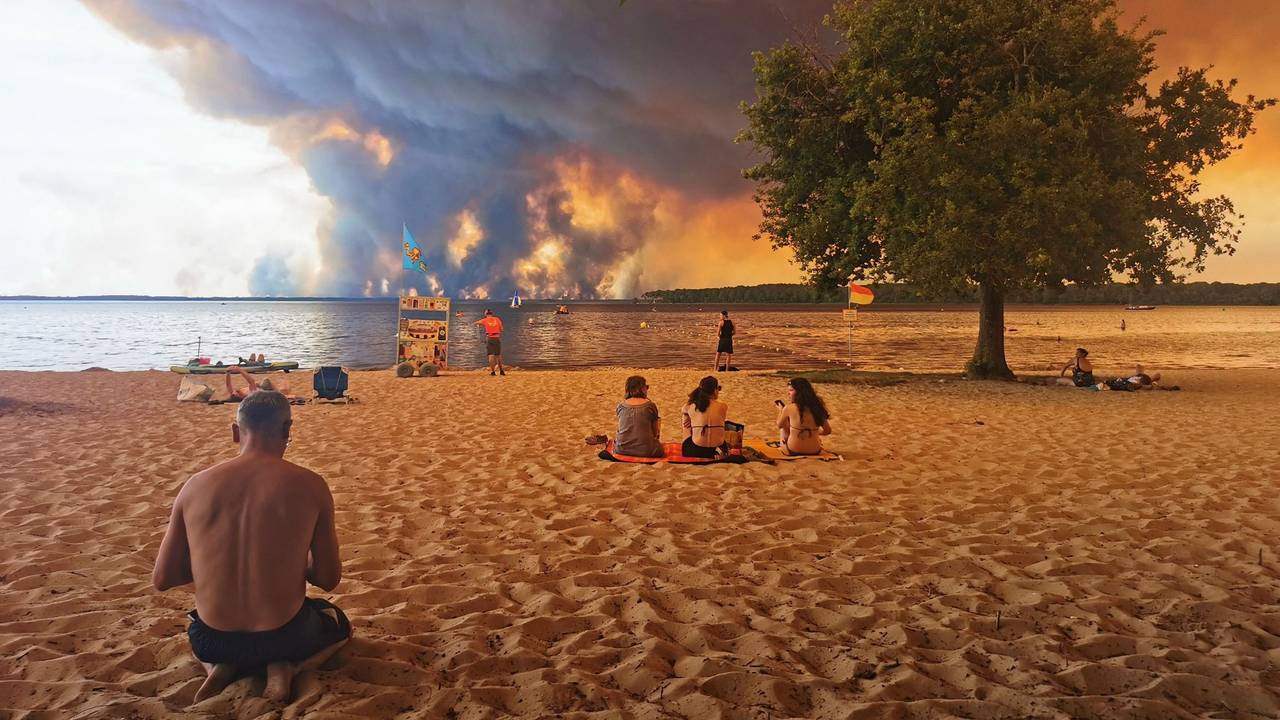 Touristen und Touristinnen beobachten vom Strand aus das Feuer. Noch ist der beliebte Urlaubsort Lacanau (Frankreich) nicht direkt von dem Waldbrand bedroht.