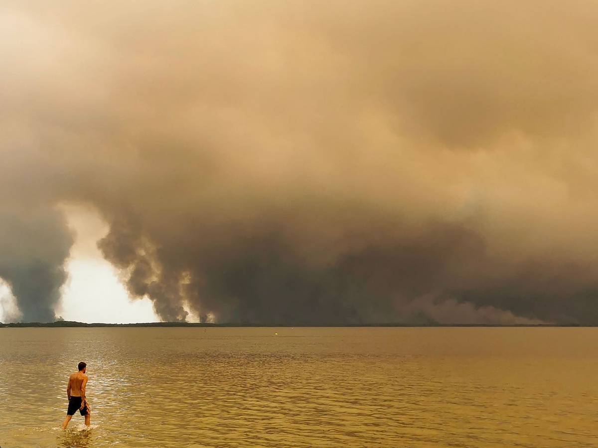 Ein Strandbesucher spaziert am Strand von Moutchic in Lacanau im Südwesten Frankreichs am Etang de Lacanau entlang, während Rauchwolken von einem Waldbrand in den Himmel aufsteigen.