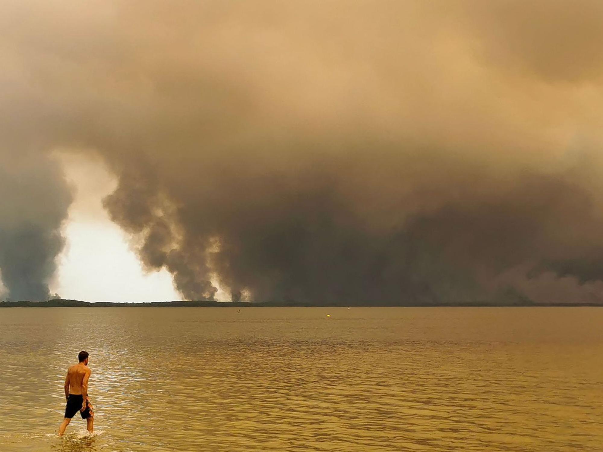 Ein Strandbesucher spaziert am Strand von Moutchic in Lacanau im Südwesten Frankreichs am Etang de Lacanau entlang, während Rauchwolken von einem Waldbrand in den Himmel aufsteigen.