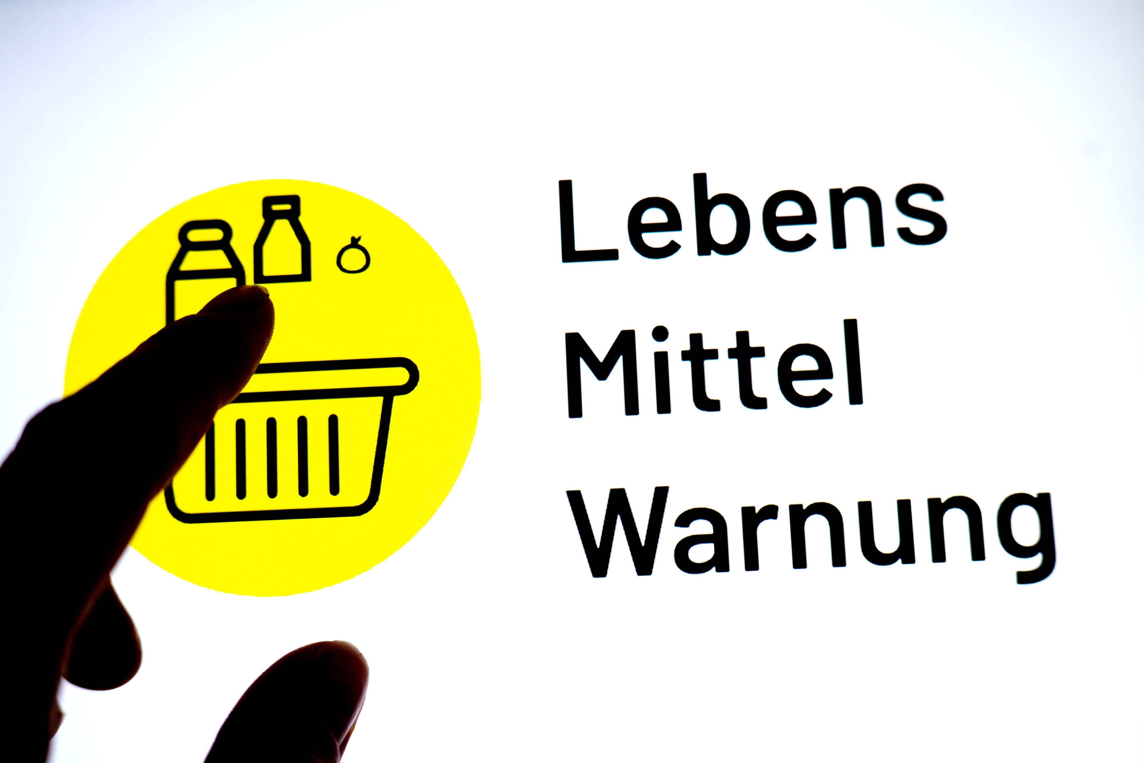 Eine Person hält einen Finger vor einen Monitor, auf dem das Logo der App „Lebensmittelwarnung“ zu sehen ist.