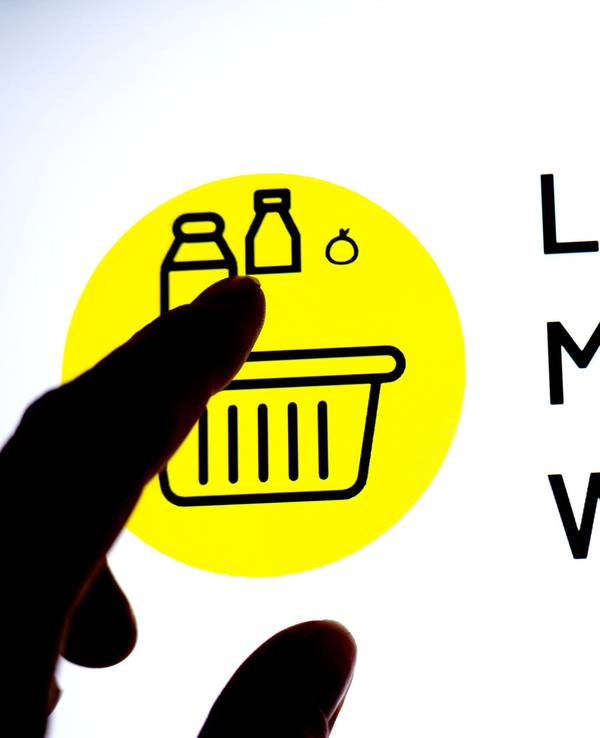 Eine Person hält einen Finger vor einen Monitor, auf dem das Logo der App „Lebensmittelwarnung“ zu sehen ist.