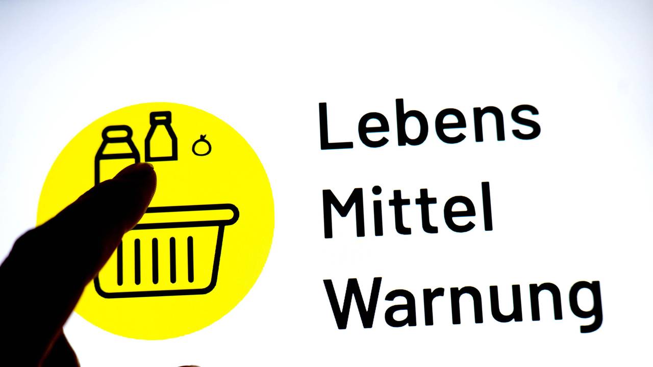 Eine Person hält einen Finger vor einen Monitor, auf dem das Logo der App „Lebensmittelwarnung“ zu sehen ist.