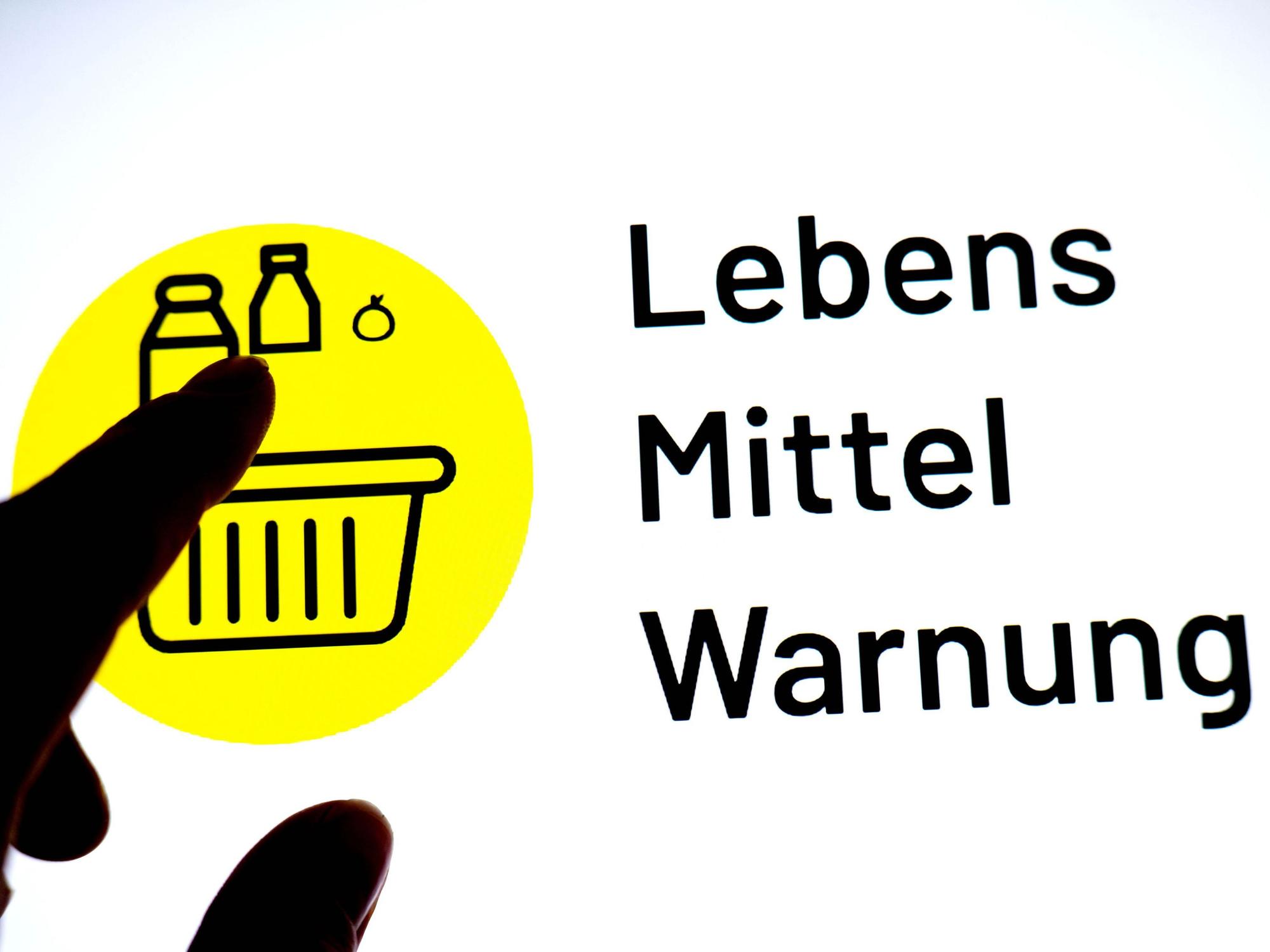 Eine Person hält einen Finger vor einen Monitor, auf dem das Logo der App „Lebensmittelwarnung“ zu sehen ist.