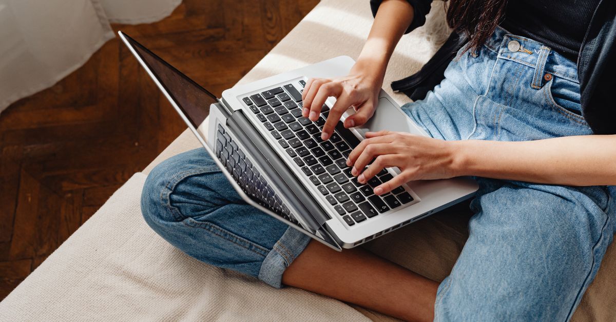 Eine Frau sitzt auf einem Sofa und tippt etwas auf ihrem Laptop.