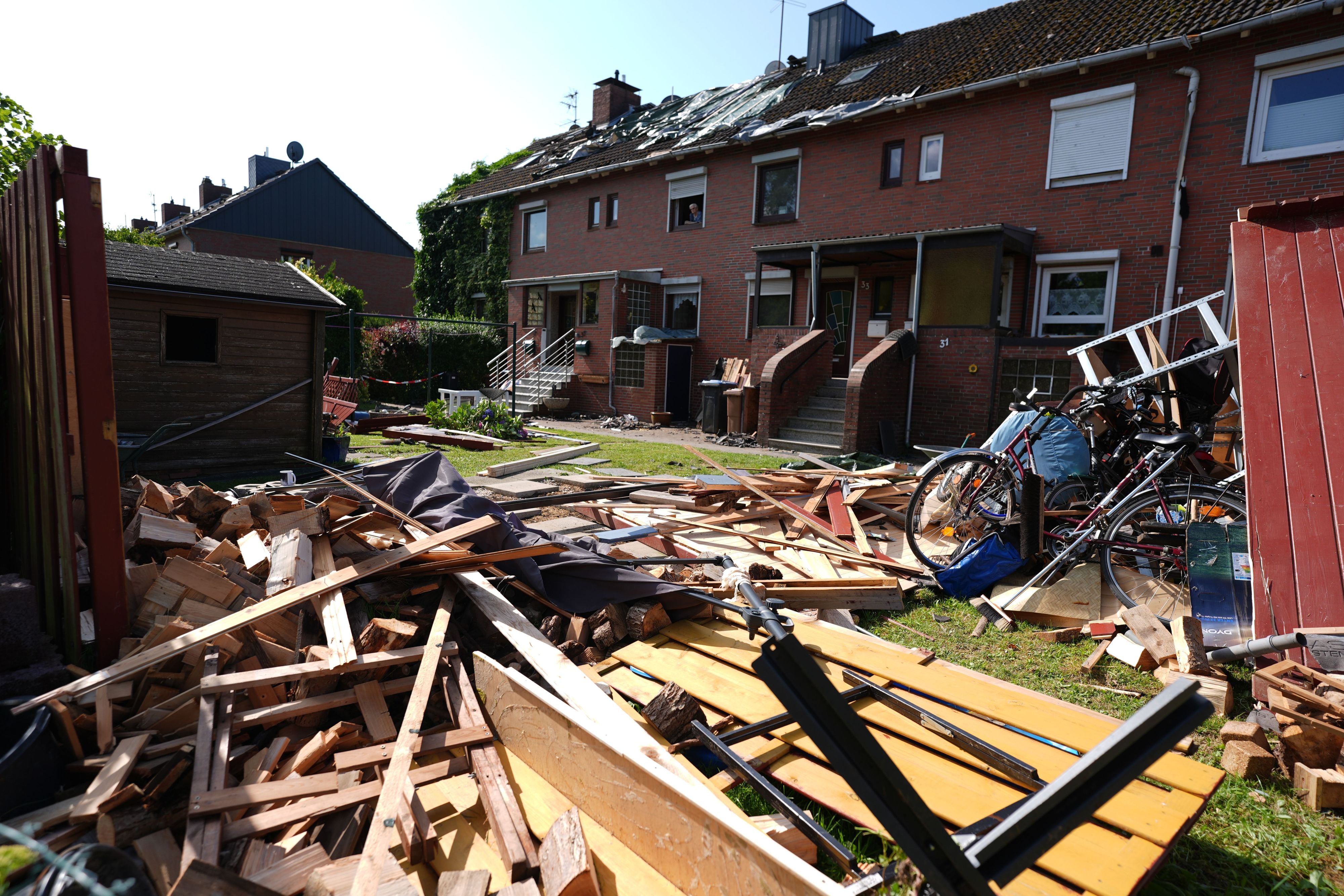 Provisorische Planen bedecken das durch ein Unwetter abgedeckte Dach eines Reihenhauses. Im Vordergrund liegen Teile einer zerstörten Gartenlaube und Dachziegel. Ein mutmaßlicher Tornado hat in und um Glückstadt in Schleswig-Holstein eine Schneise der Verwüstung geschlagen und nach ersten Schätzungen Schäden in sechs- bis siebenstelliger Höhe verursacht.