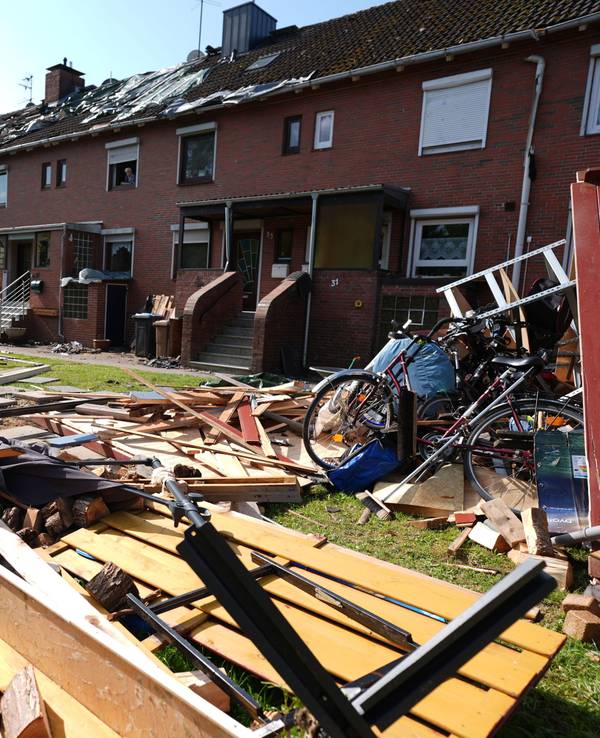 Provisorische Planen bedecken das durch ein Unwetter abgedeckte Dach eines Reihenhauses. Im Vordergrund liegen Teile einer zerstörten Gartenlaube und Dachziegel. Ein mutmaßlicher Tornado hat in und um Glückstadt in Schleswig-Holstein eine Schneise der Verwüstung geschlagen und nach ersten Schätzungen Schäden in sechs- bis siebenstelliger Höhe verursacht.
