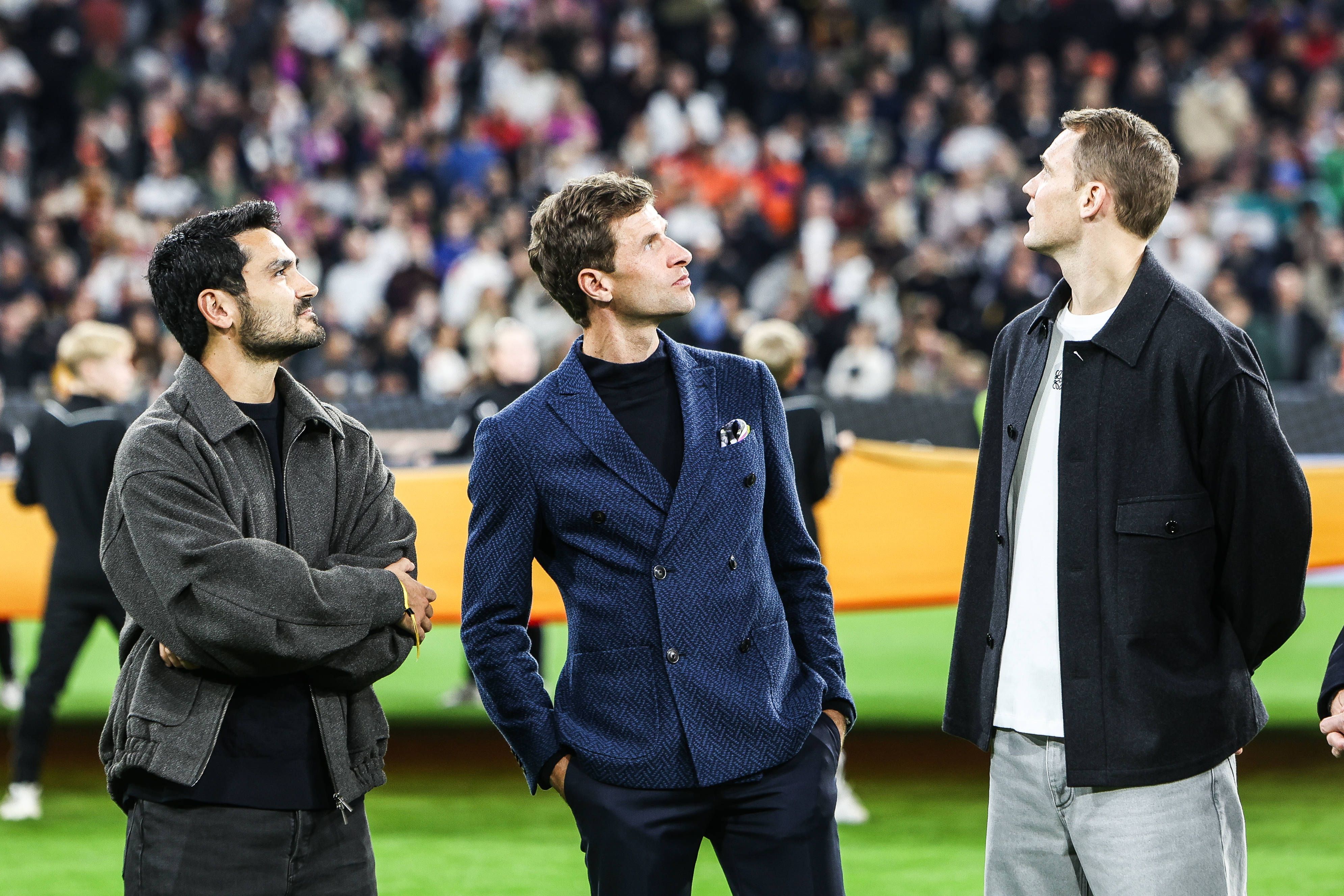 Ilkay Gündogan, Thomas Müller und Manuel Neuer stehen vor dem Spiel auf dem Platz und schauen nach oben.
