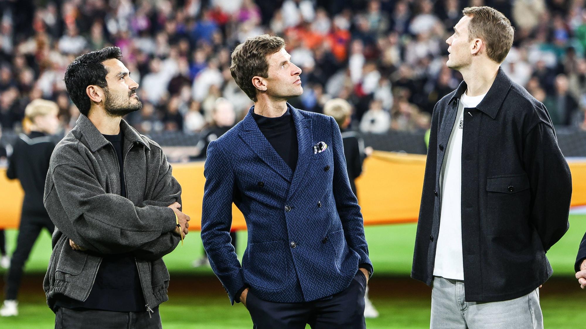 Ilkay Gündogan, Thomas Müller und Manuel Neuer stehen vor dem Spiel auf dem Platz und schauen nach oben.